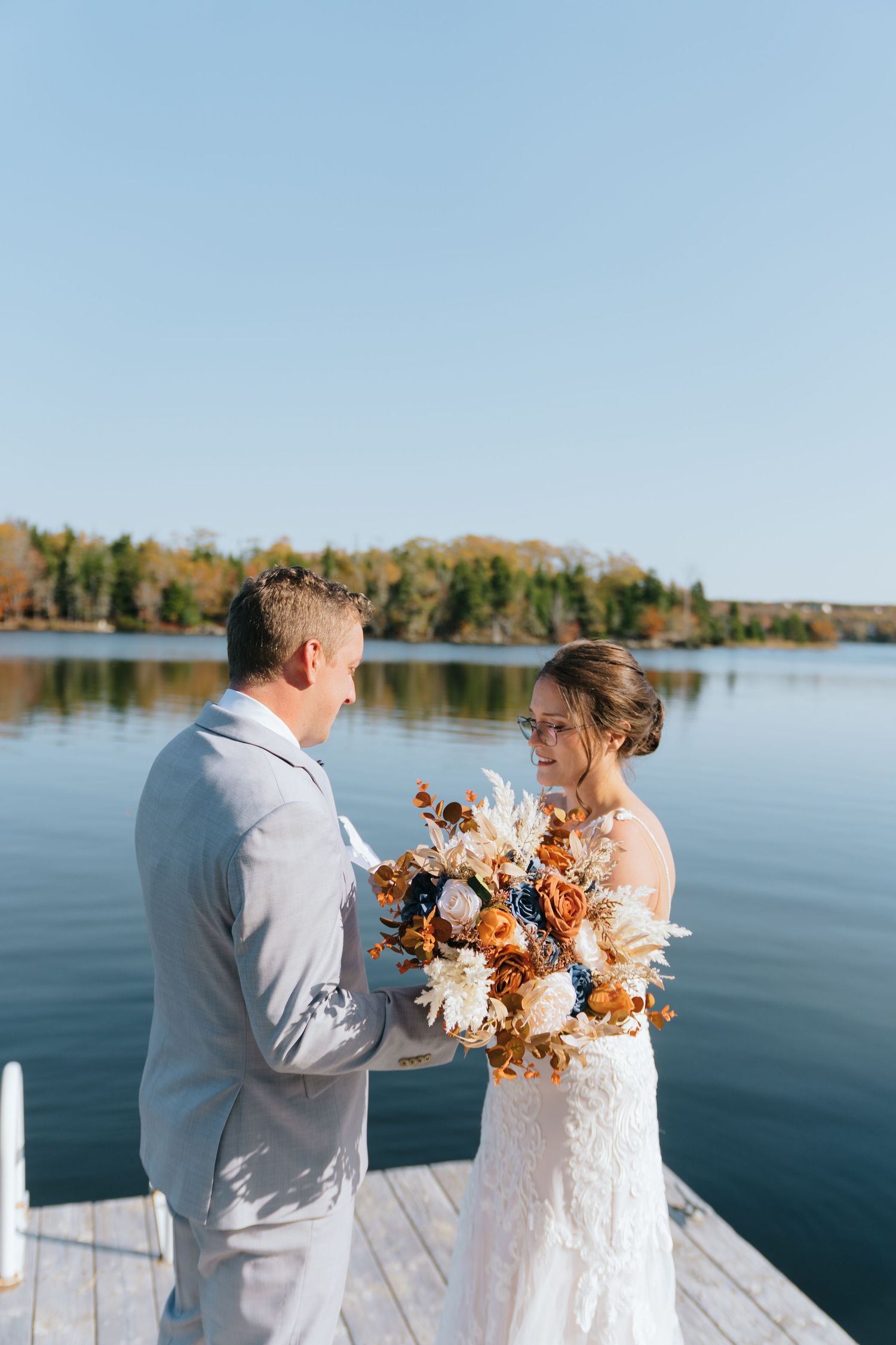 A lakeside wedding moment on a dock with fall foliage in the background.