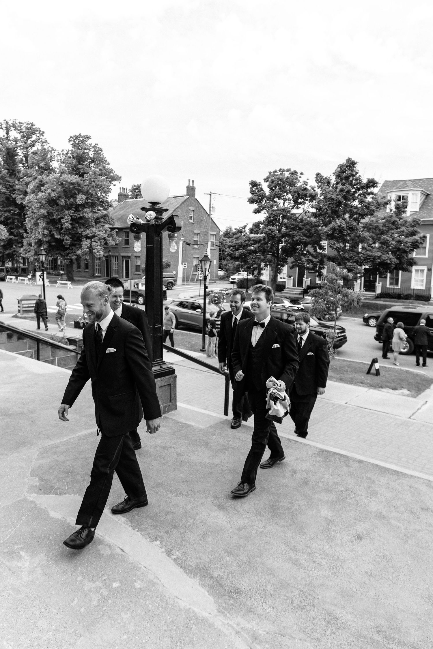 Black and white photo of wedding party members walking down a city sidewalk in formal attire.