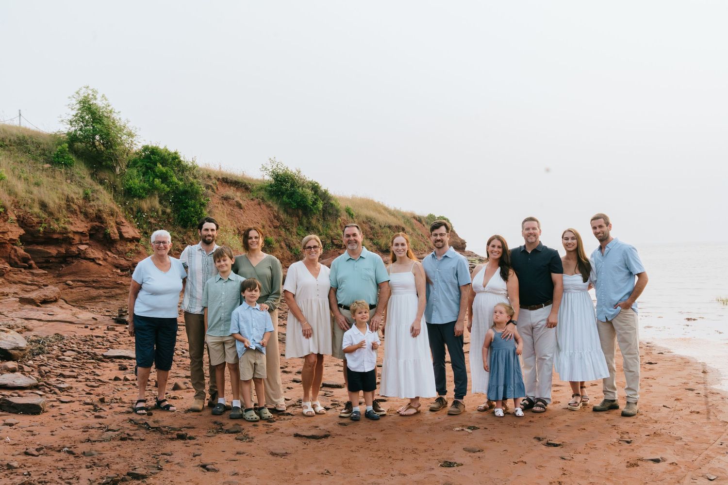 Family group dressed in coordinating blue and white outfits posing on a rocky beach.