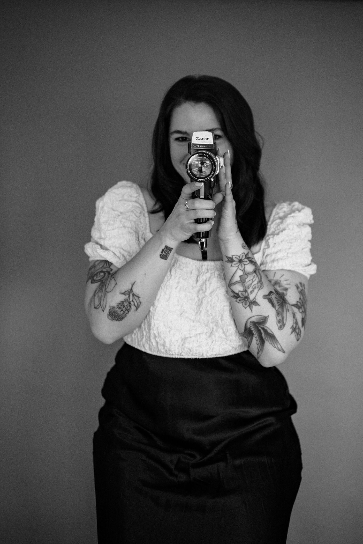 Photographer in white top and black skirt holding vintage camera in studio setting.