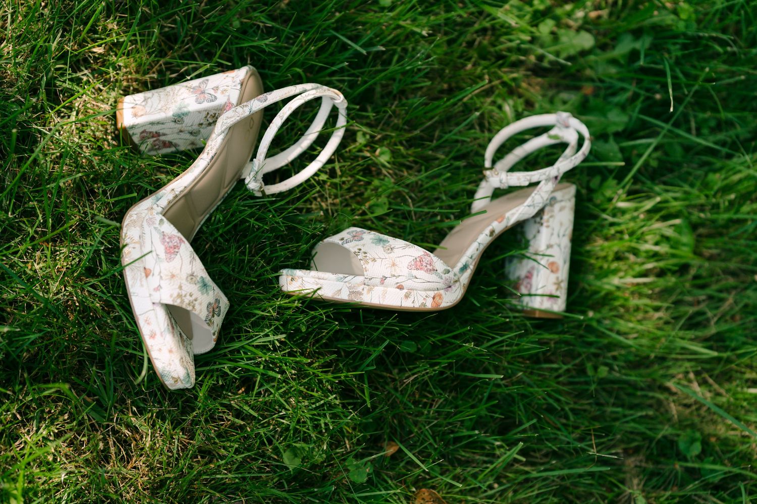 Floral print block heel sandals with ankle straps resting on lush green grass.