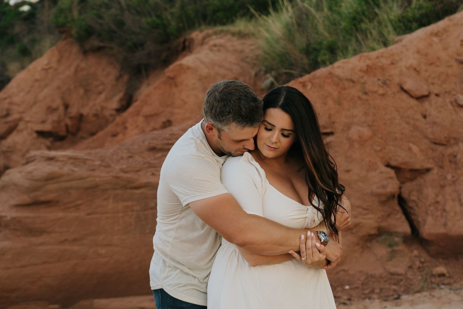 A couple shares an intimate moment against red rock formations at sunset.