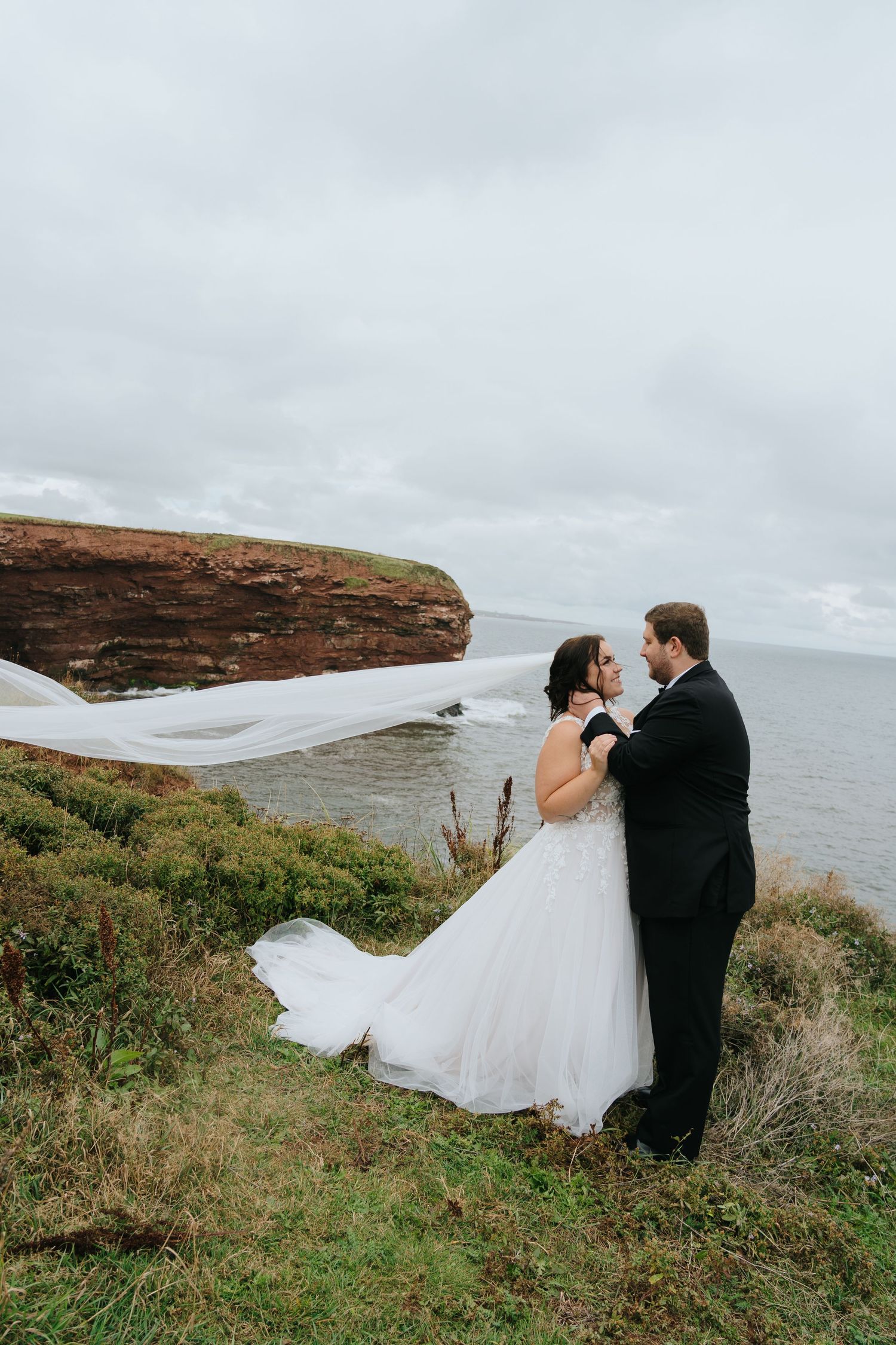 A couple shares a romantic moment on a scenic coastal cliff overlooking the ocean on their wedding day.