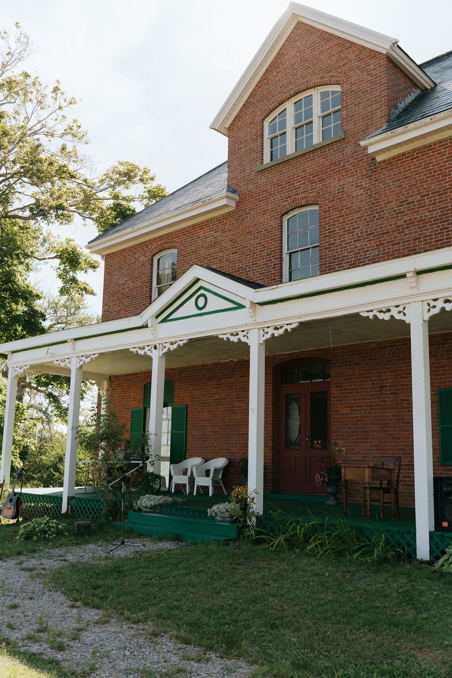 A red brick building with white columns and green shutters features a covered porch with white rocking chairs.