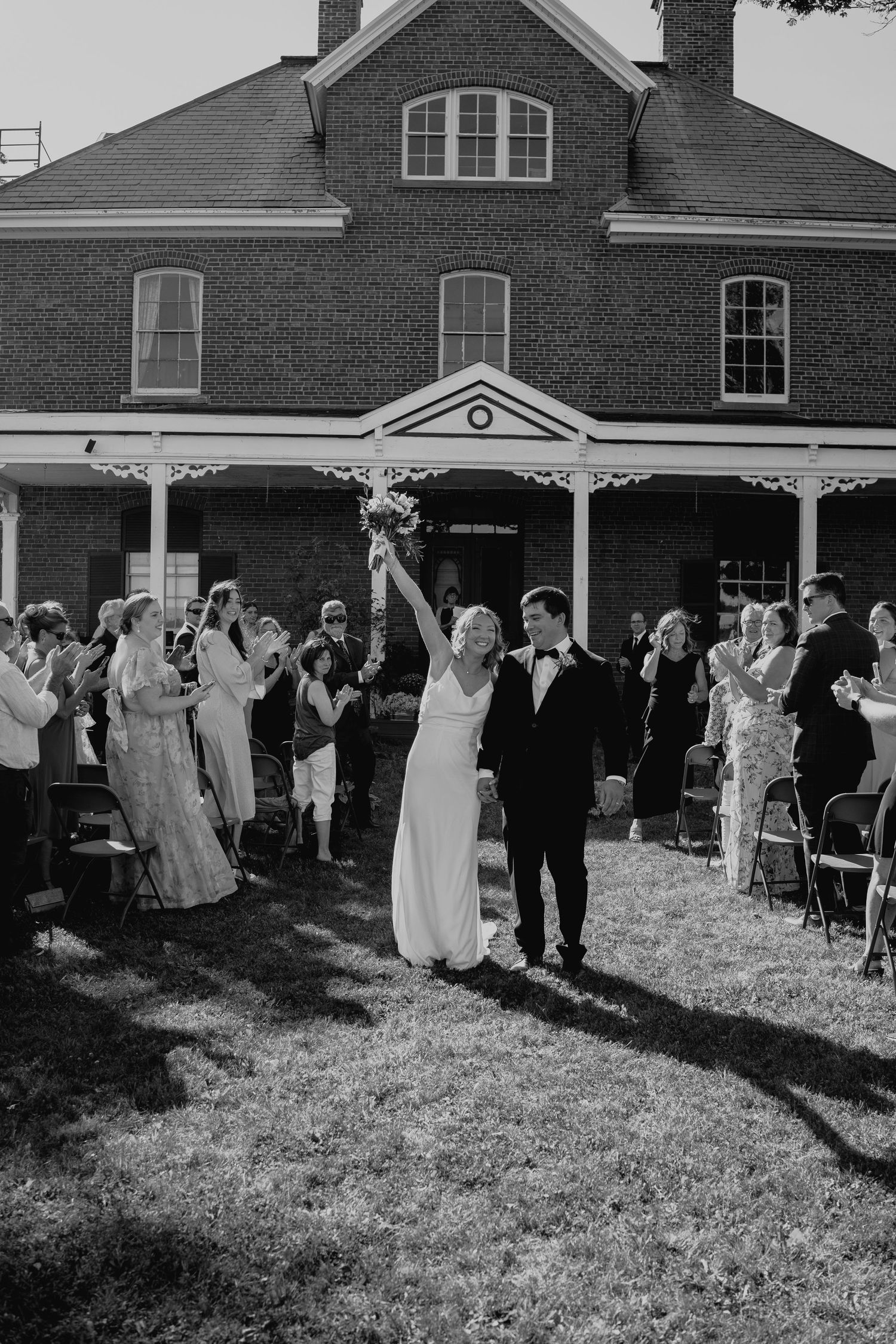 A joyous wedding celebration outside a historic brick building with guests cheering.