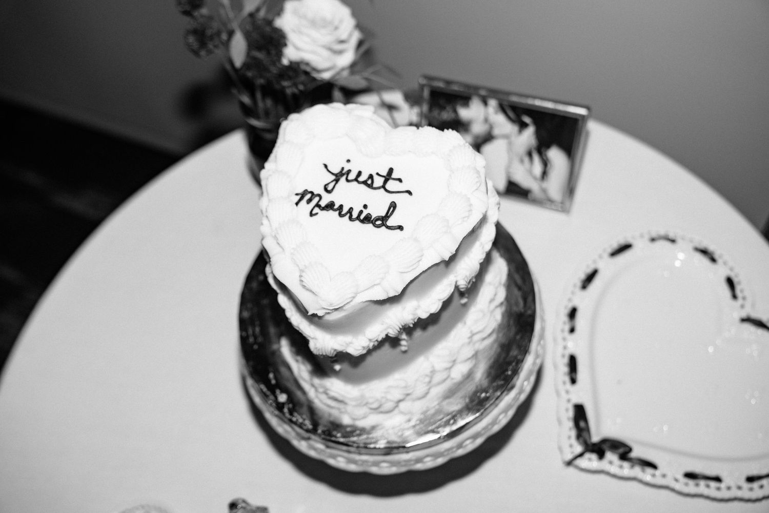 Black and white photo of a two-tier wedding cake with just married written on top, displayed on a round table.