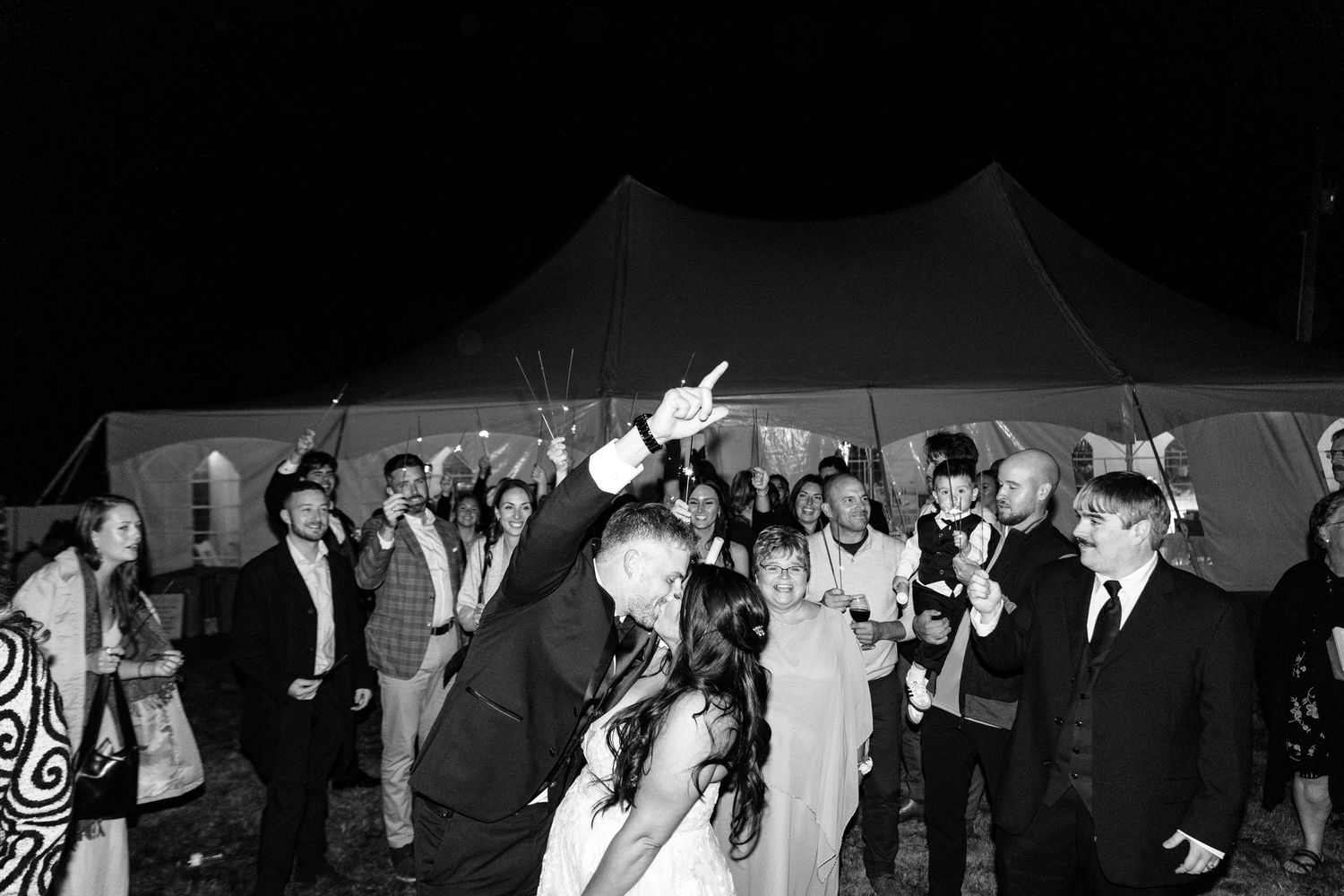 A nighttime wedding reception under a tent with guests dancing and celebrating.