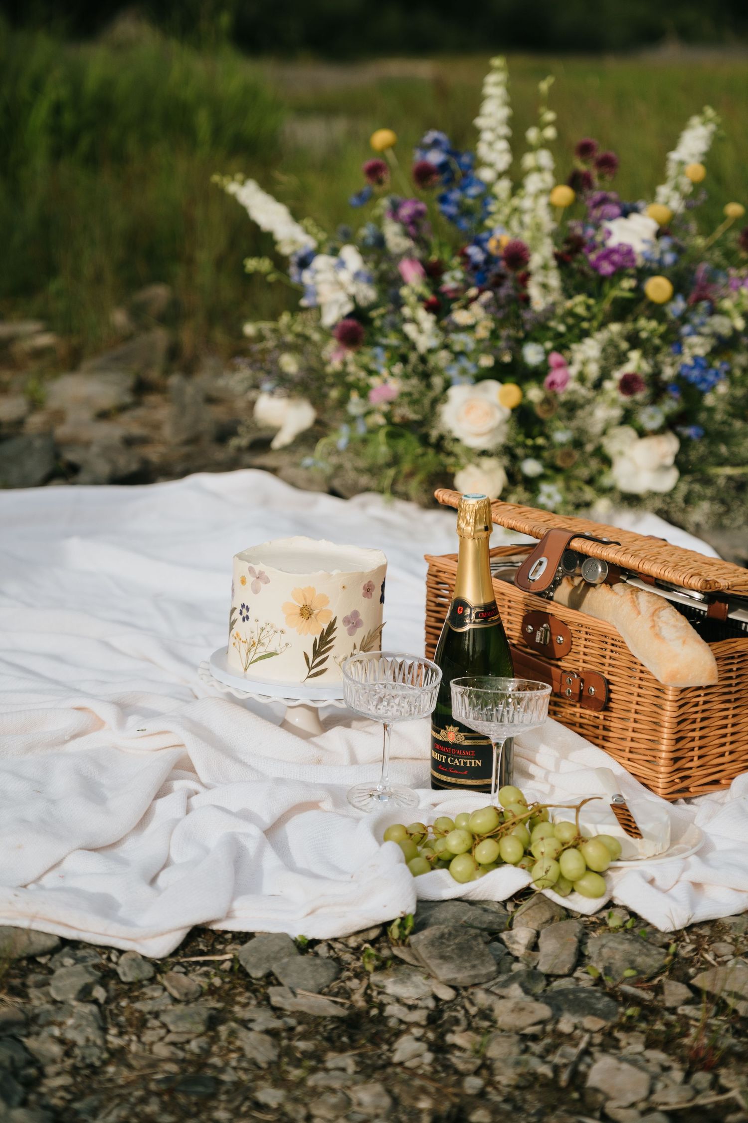 A romantic picnic setup in Alaska with flowers, basket, and refreshments on a white blanket.