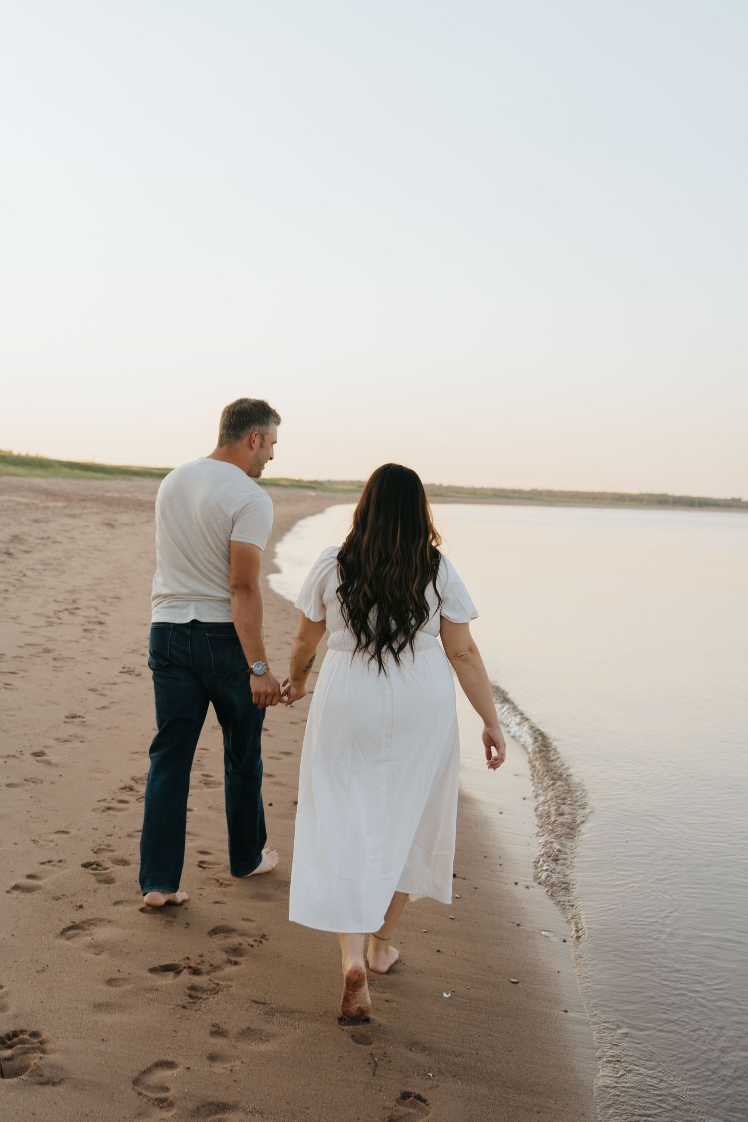 A couple walks along the shoreline during a peaceful sunset.