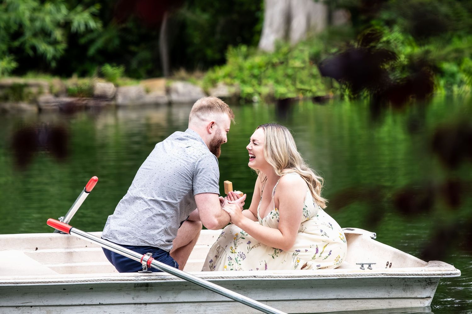 A couple shares a romantic moment in a rowboat on a serene lake surrounded by lush greenery.