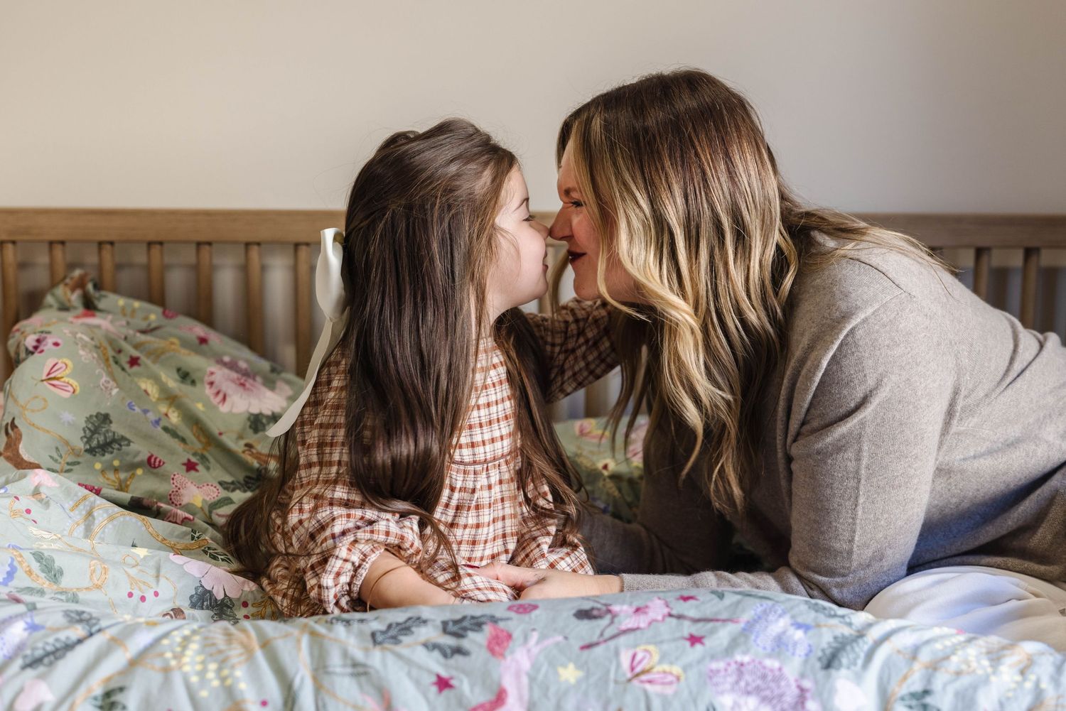 Mother and daughter sharing a tender nose-to-nose moment while sitting together on a floral bedspread.