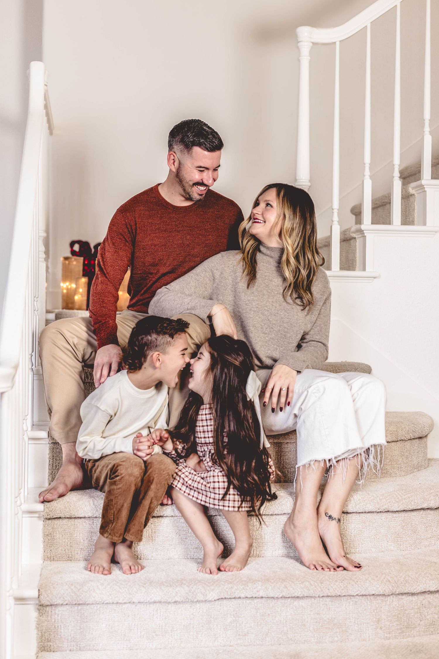 Happy family of four sitting on carpeted stairs at home, parents smiling at each other while children play together.