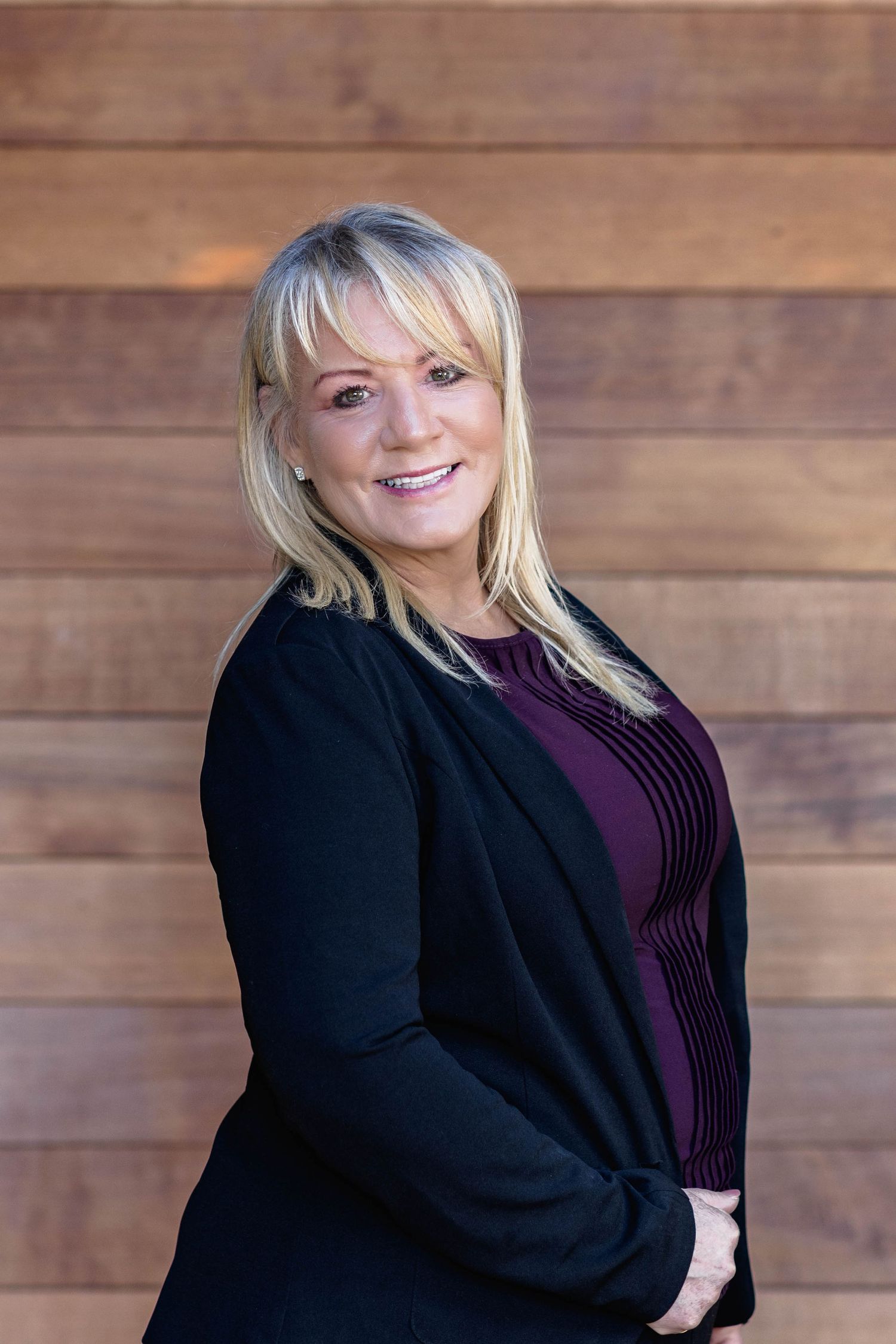 Professional headshot series showing someone in a black blazer and purple top against a wooden wall background.