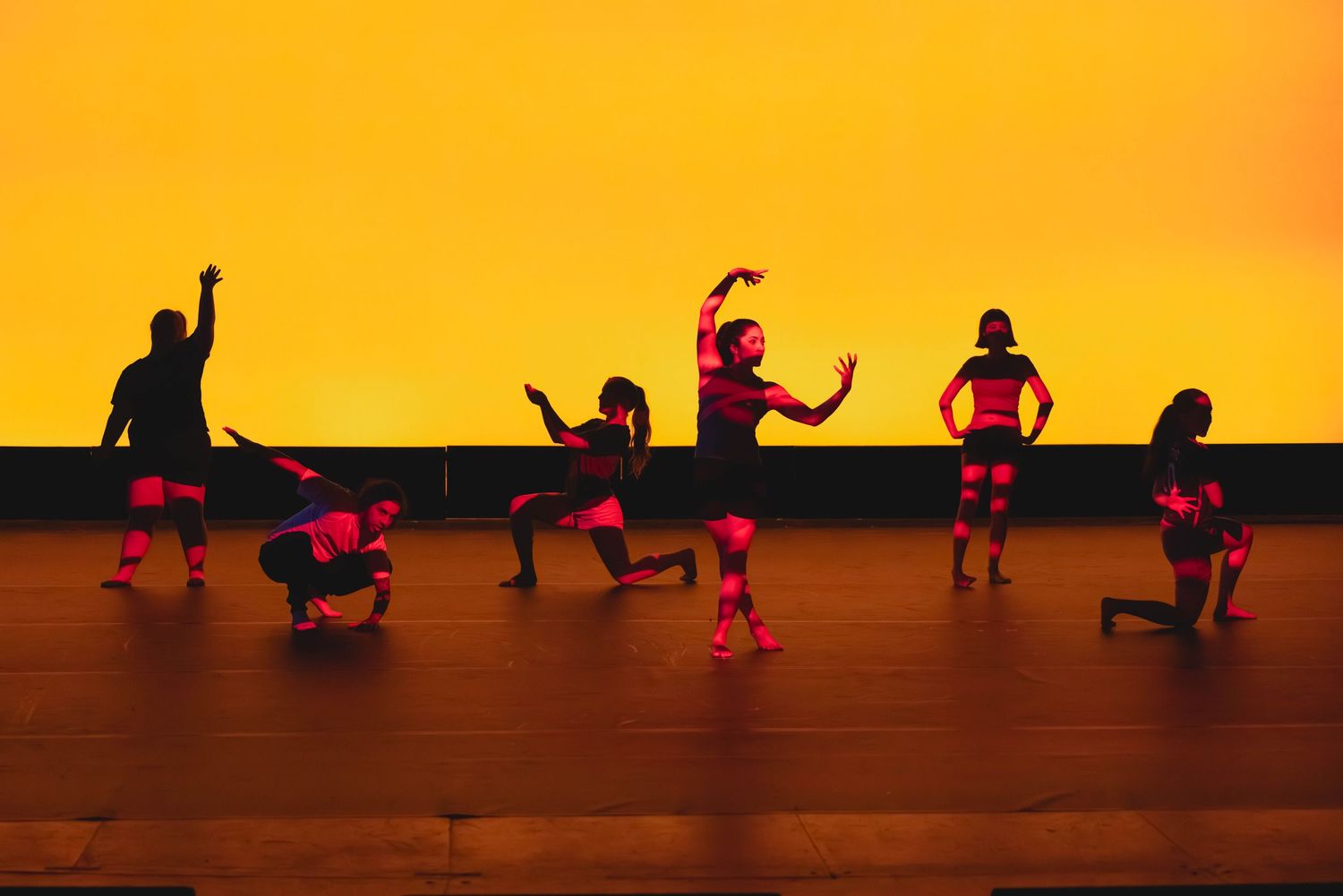 Silhouetted dancers performing on a stage bathed in warm orange light during a dance recital.