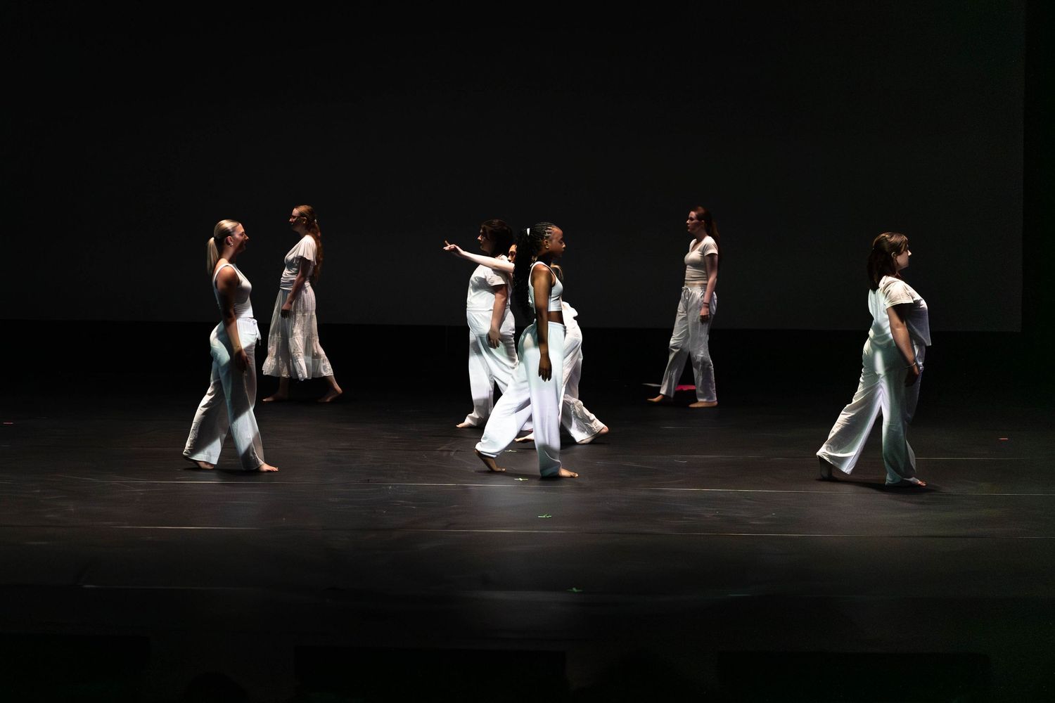 Dancers in white costumes perform on a dark stage during a contemporary dance performance.