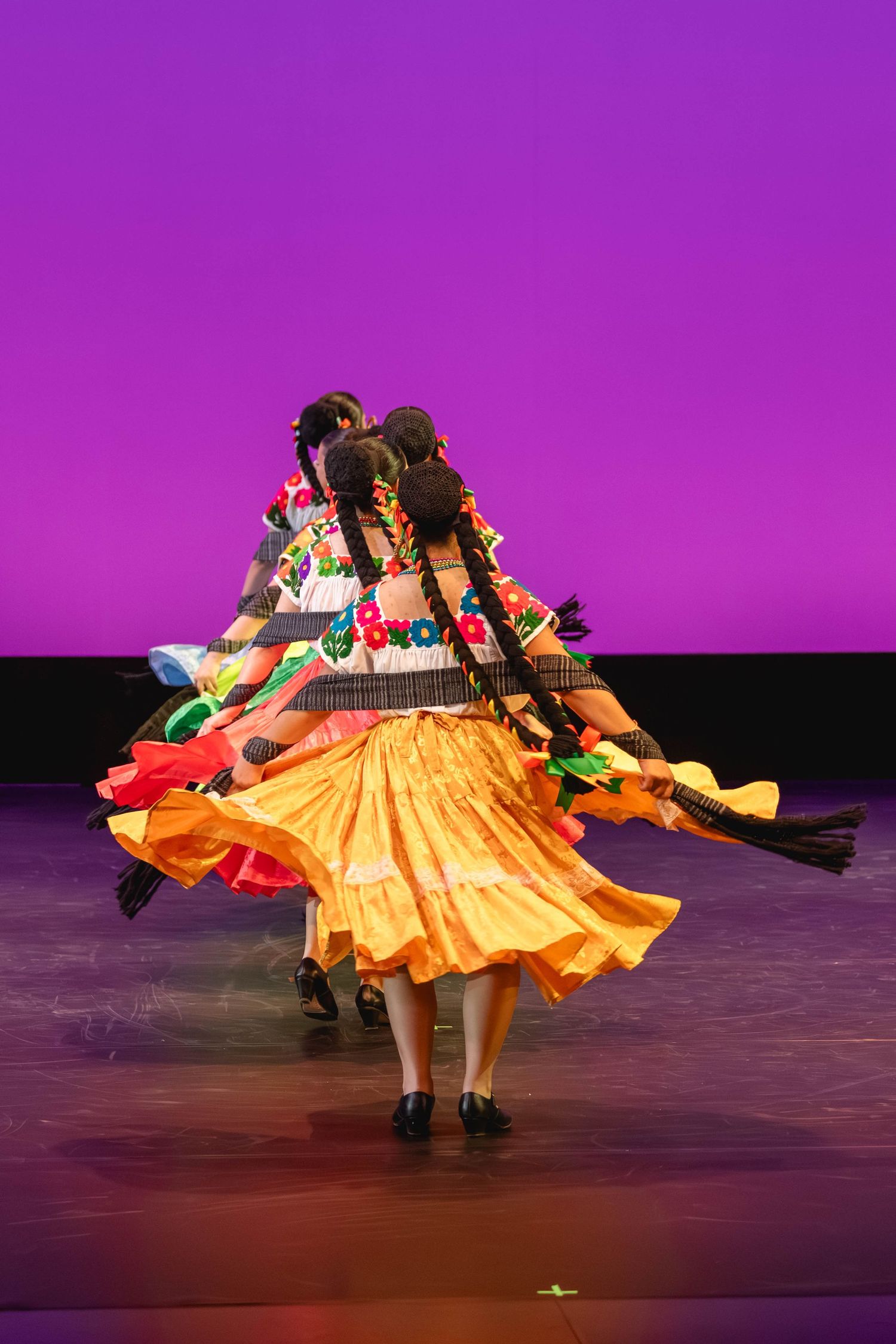 Folkloric dancer in vibrant traditional costume with colorful embroidery and flowing orange skirt performing on stage.