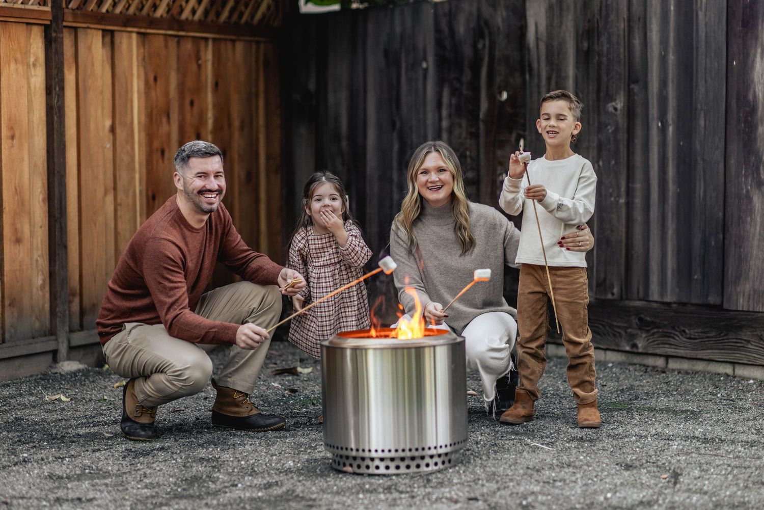 Family of four roasting marshmallows around a Solo Stove fire pit outdoors, smiling and enjoying a cozy gathering.