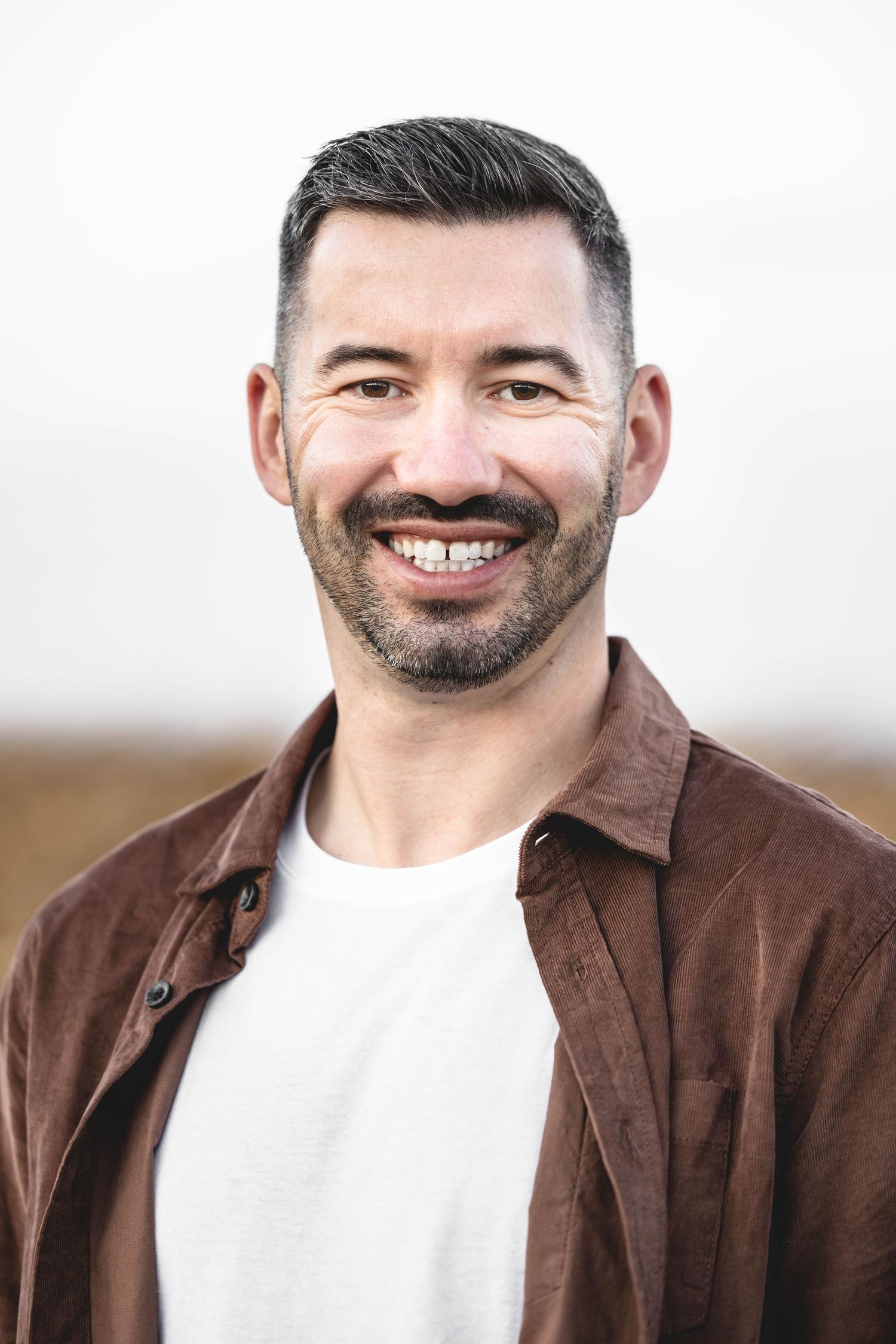 Person wearing a brown leather jacket and white t-shirt smiles warmly at the camera.
