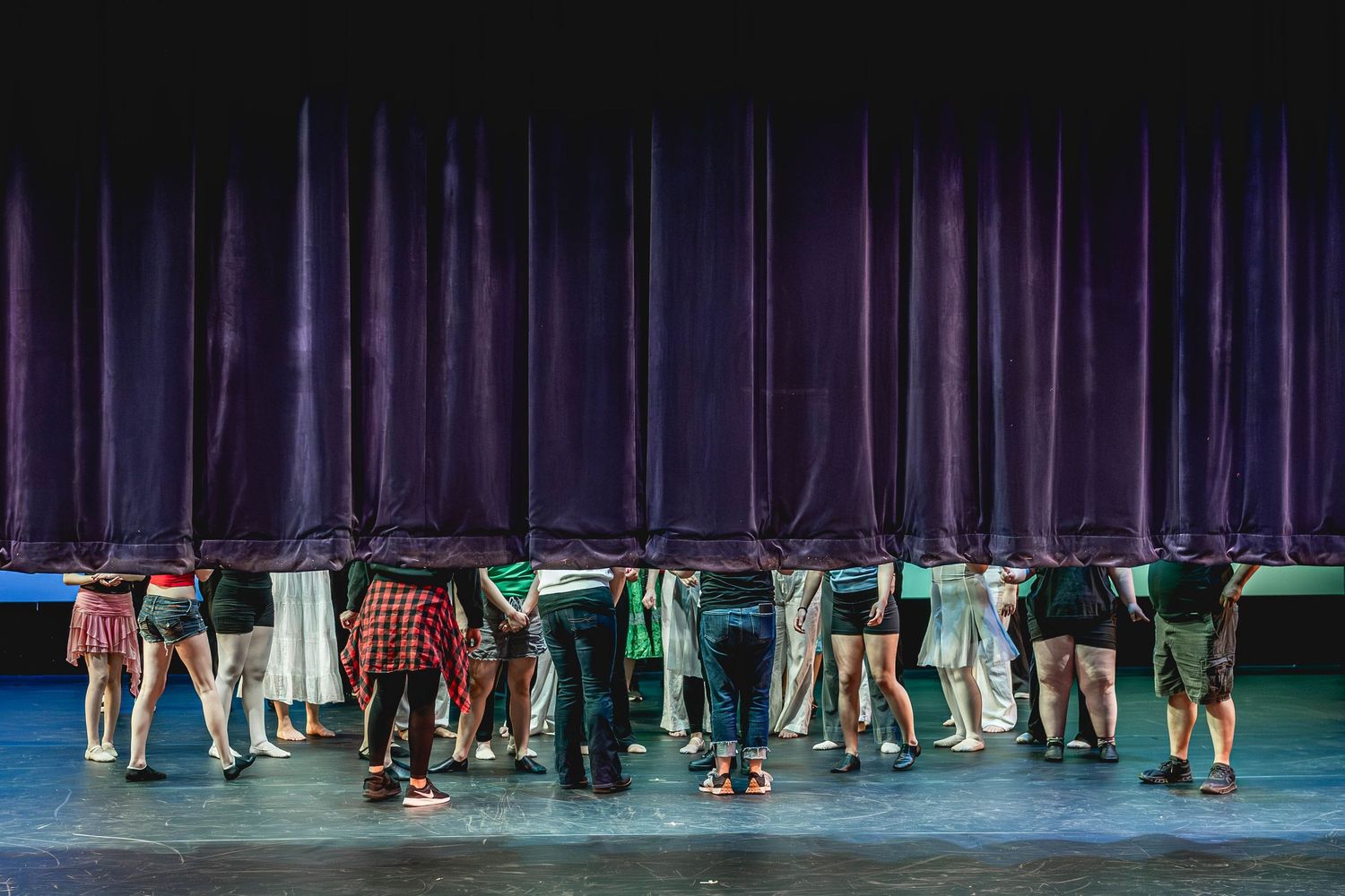 Group of performers standing in a line on stage in front of a blue curtain during a theater performance.