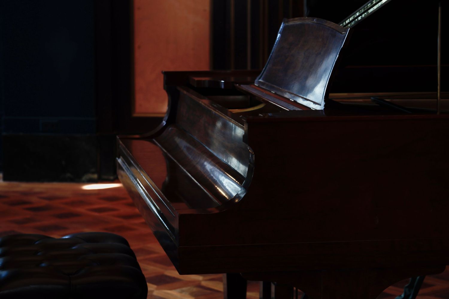 A grand piano with an open lid stands on stage in dramatic lighting with dark shadows.