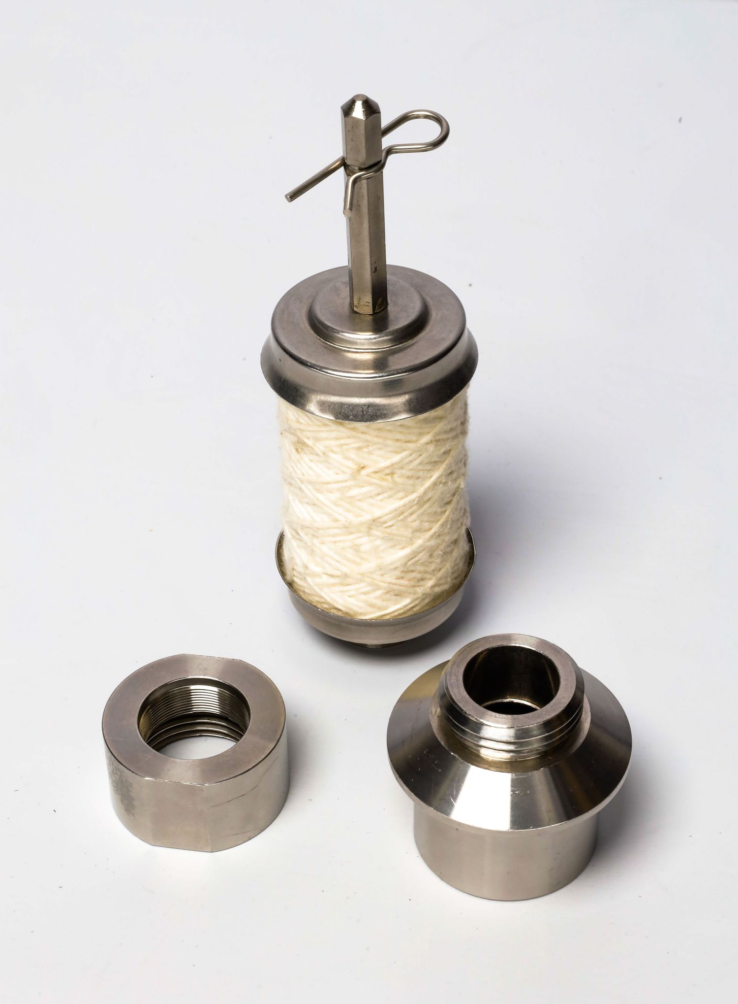 Metal thread spool holder with cream colored thread and detachable components on white background.