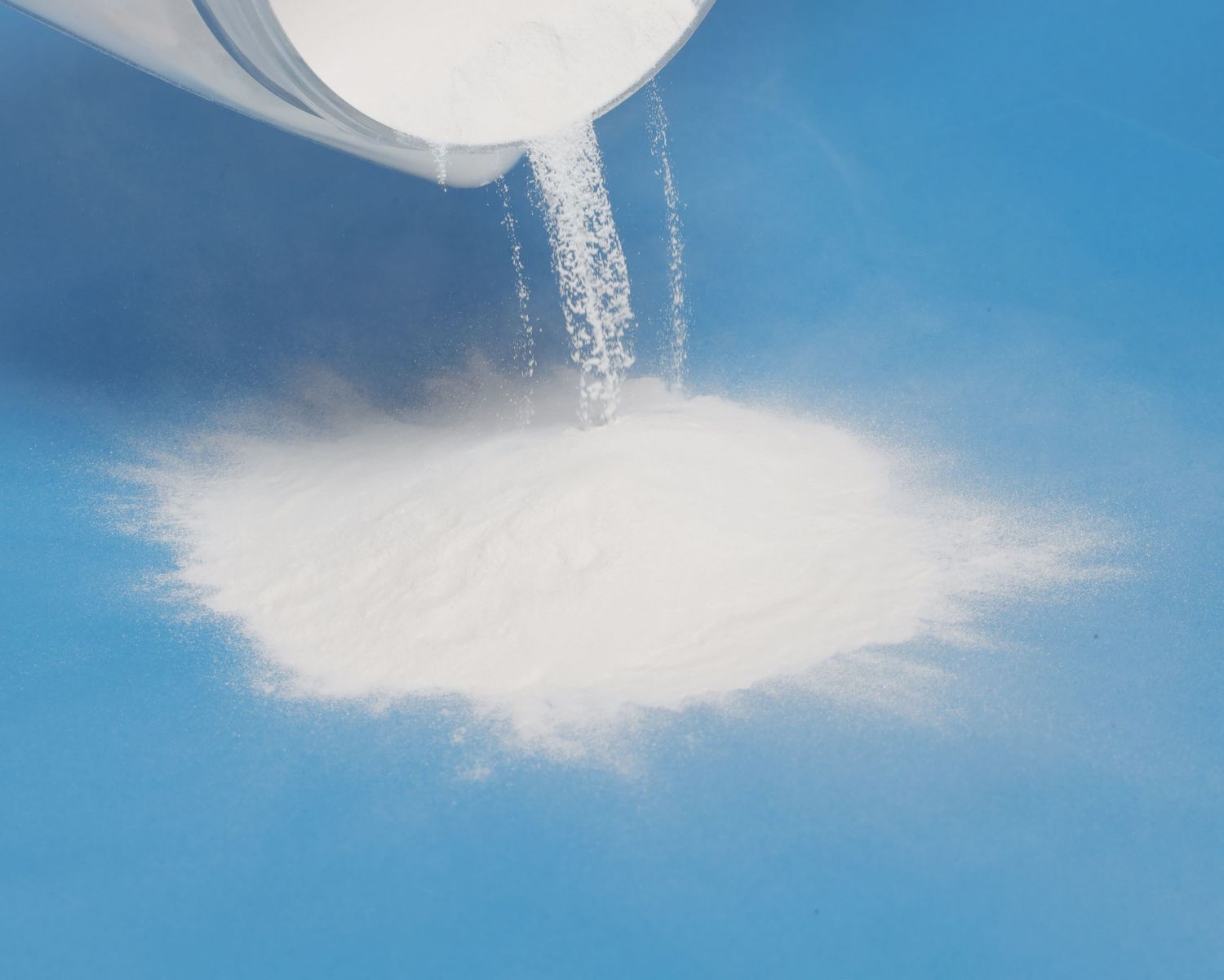 White granulated sugar being poured onto a blue surface in a close-up photography shot.