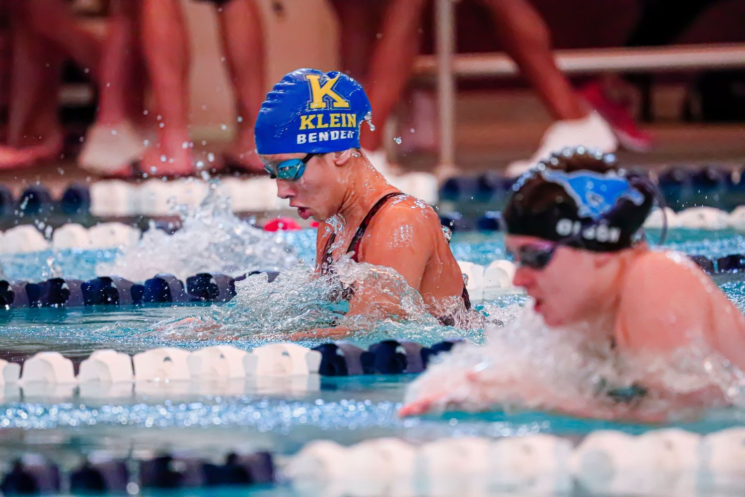 Competitive swimmer in blue cap executes breaststroke technique during swim meet race.