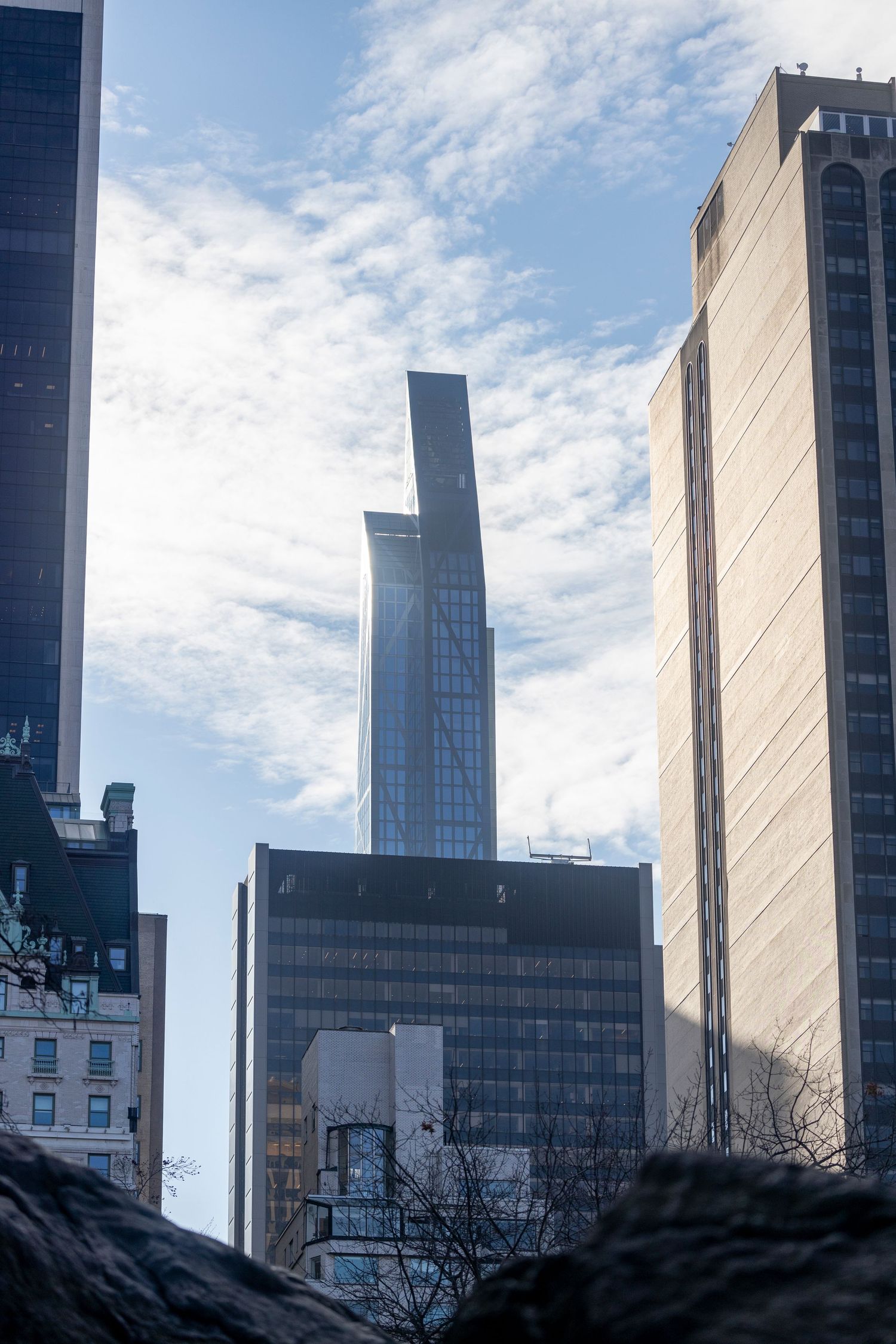 Modern skyscrapers rise against a cloudy blue sky in Manhattan, featuring contemporary glass and steel architecture.