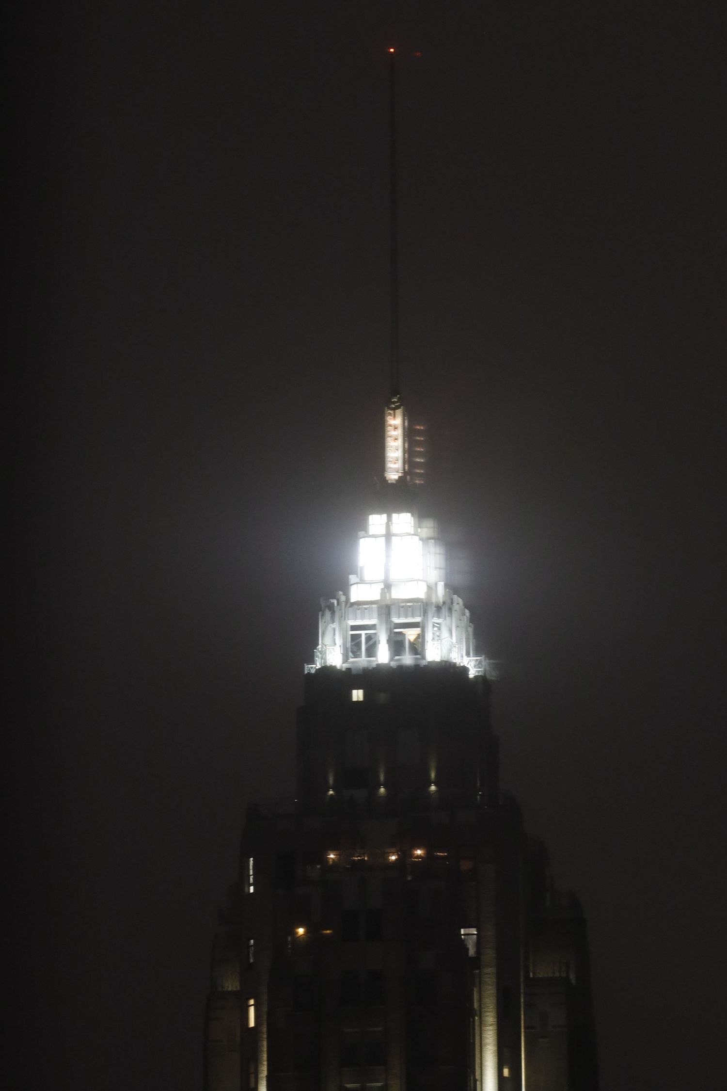 Illuminated art deco tower spire glowing against dark night sky.