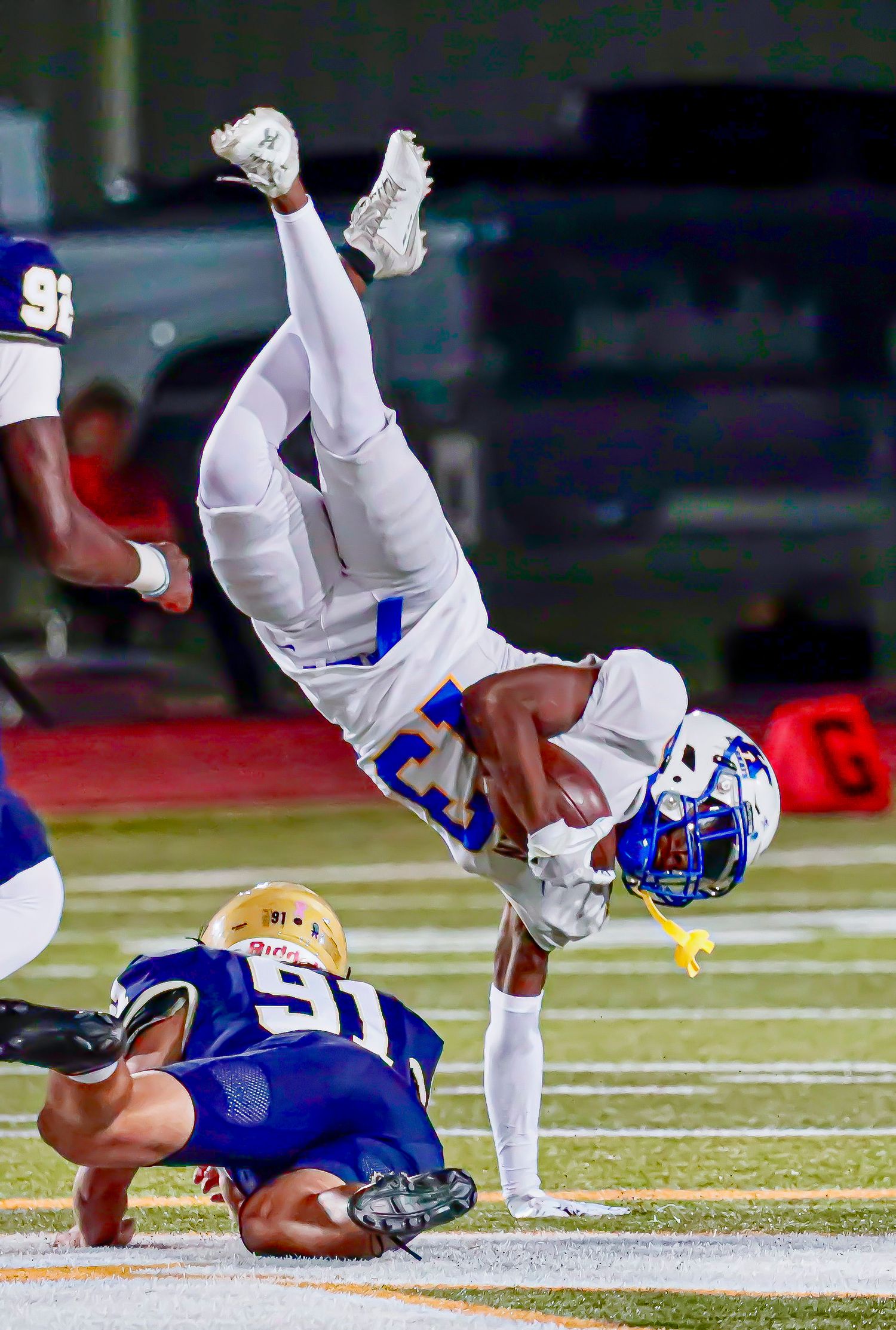 Football player performs an acrobatic flip during a game with dramatic lighting on the field.