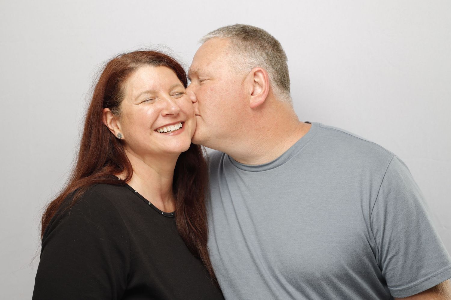 A playful intimate moment between a couple wearing black and grey shirts against a light background.