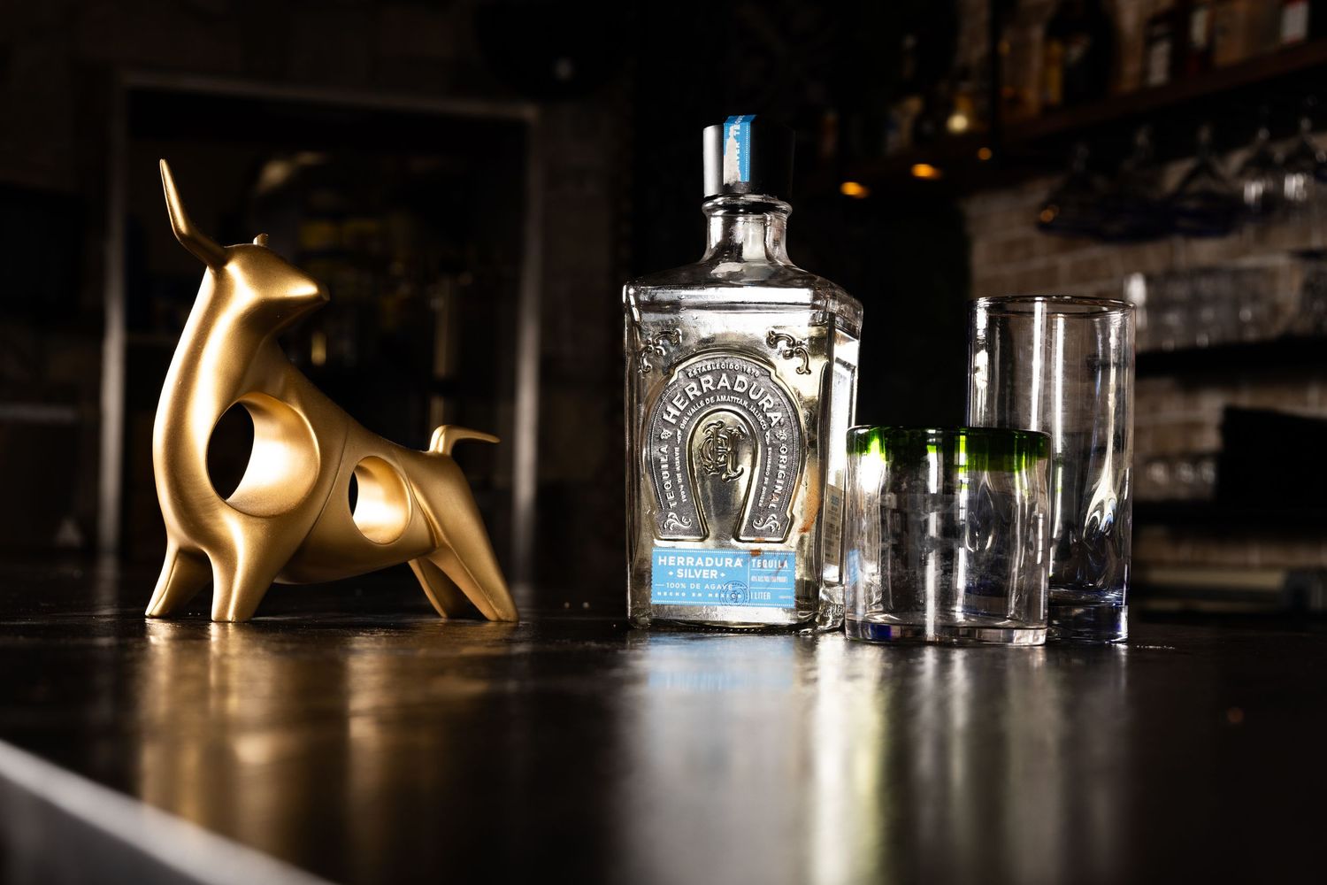 A bottle of gin with a horseshoe design sits next to a decorative gold animal figure on a dark surface.