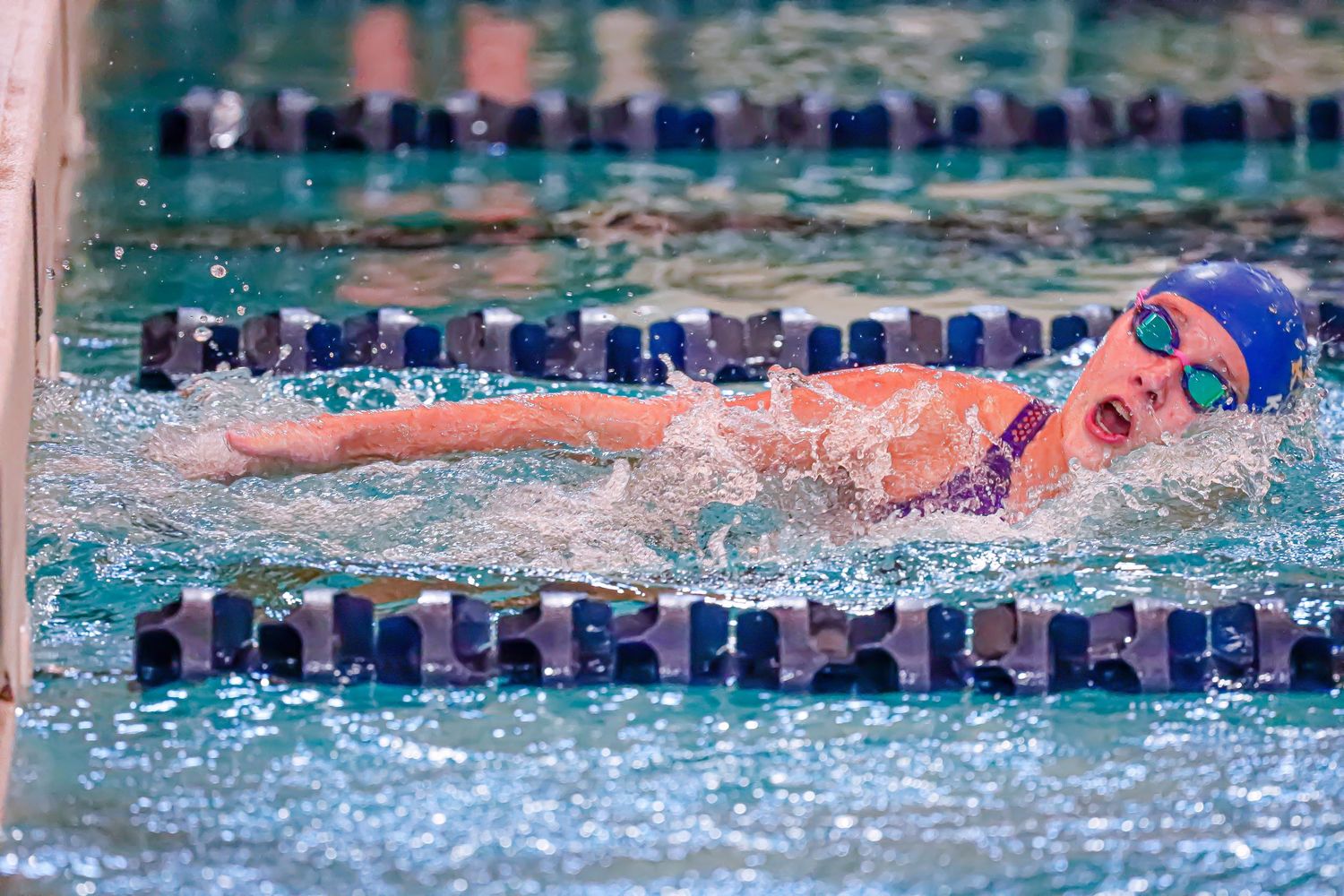 Swimmer performs freestyle stroke during competitive race with splashing water in pool lane.