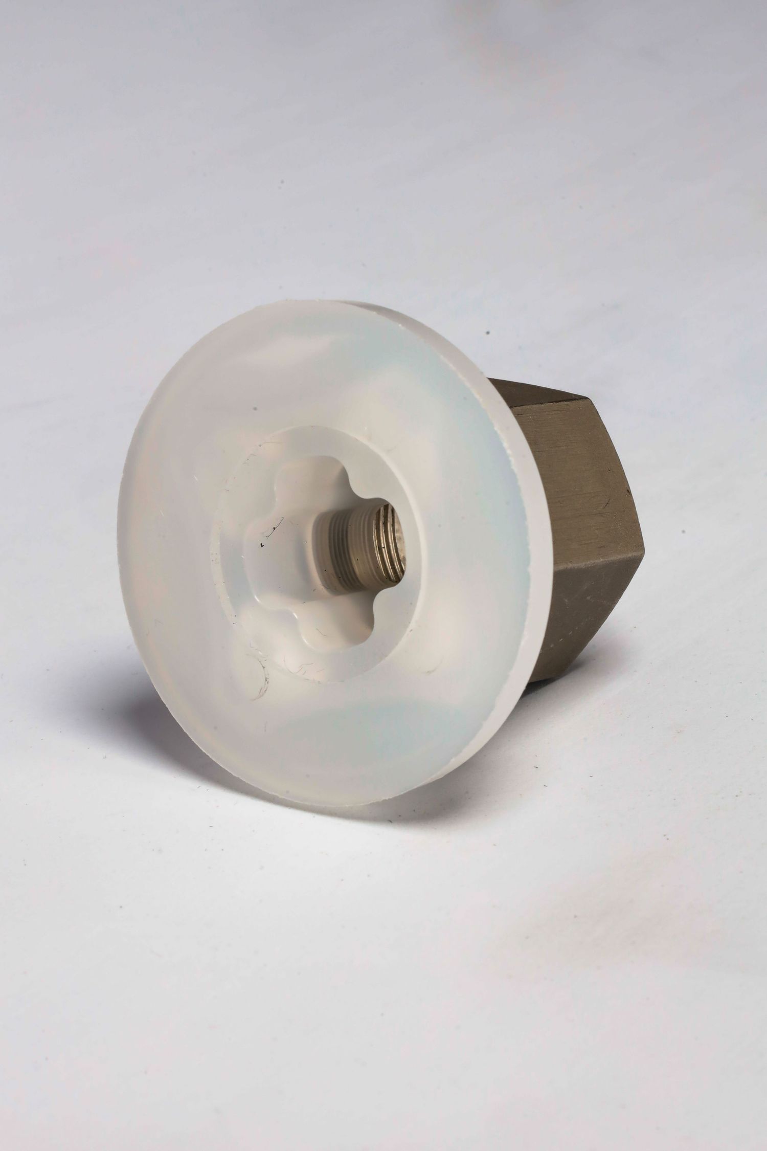 A white plastic screw or bolt head with a large circular washer against a plain light background.