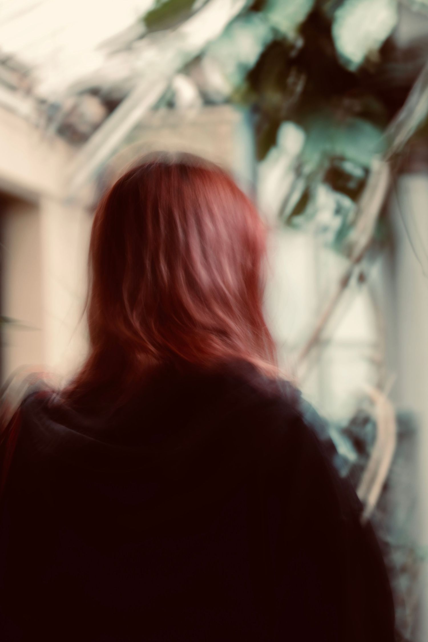 Blurry portrait showing the back of someone with red hair wearing a dark jacket.