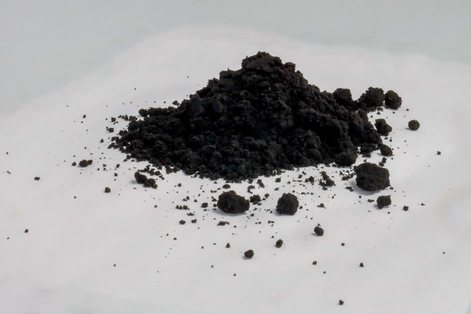 A pile of black powdery substance scattered on a white surface.