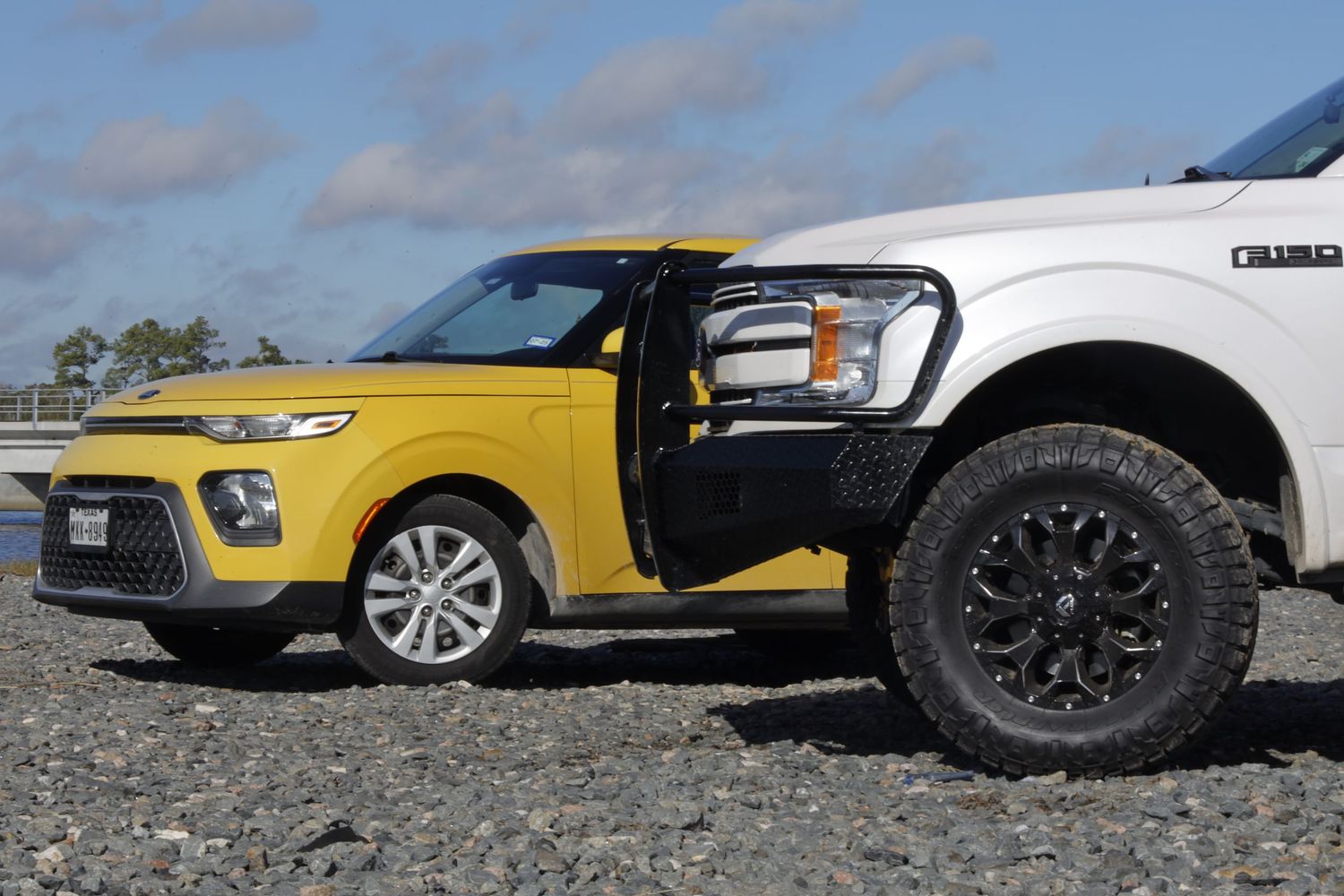A bright yellow Kia Soul parked next to a white pickup truck displaying contrasting vehicle sizes and styles.