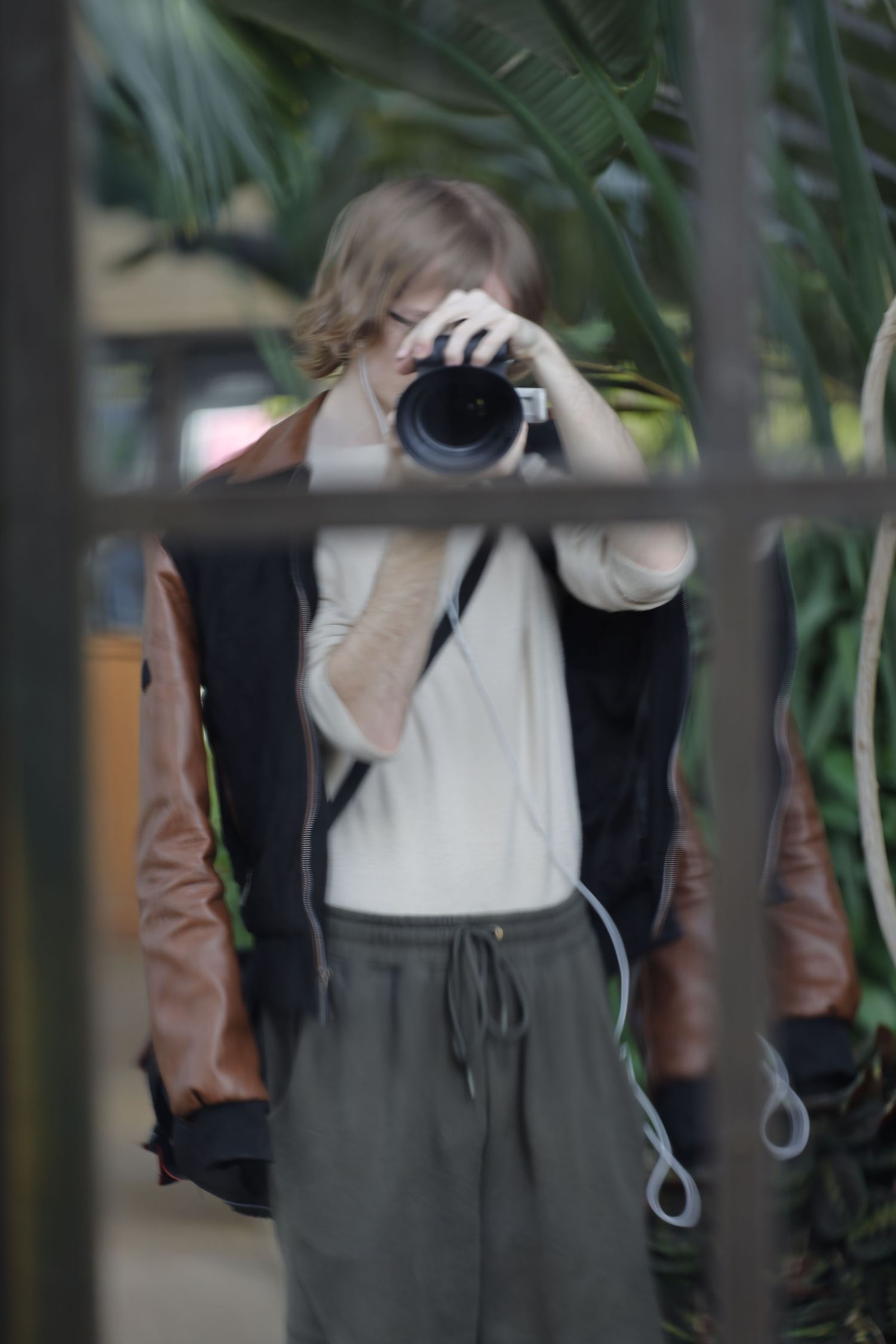 Photographer taking picture through window with tropical plants in foreground.