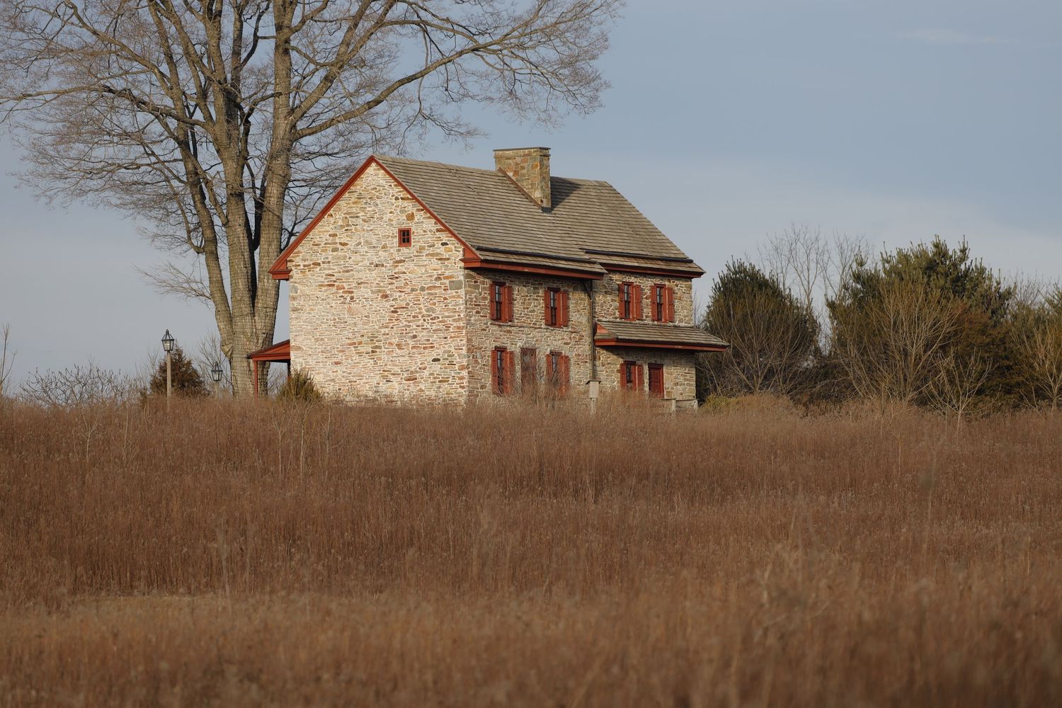 Historic stone farmhouse stands in a brown winter field with bare trees in the background.