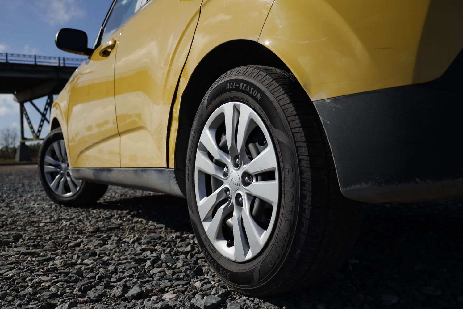 Close up view of an alloy wheel and tire on a yellow SUV parked on gravel ground.