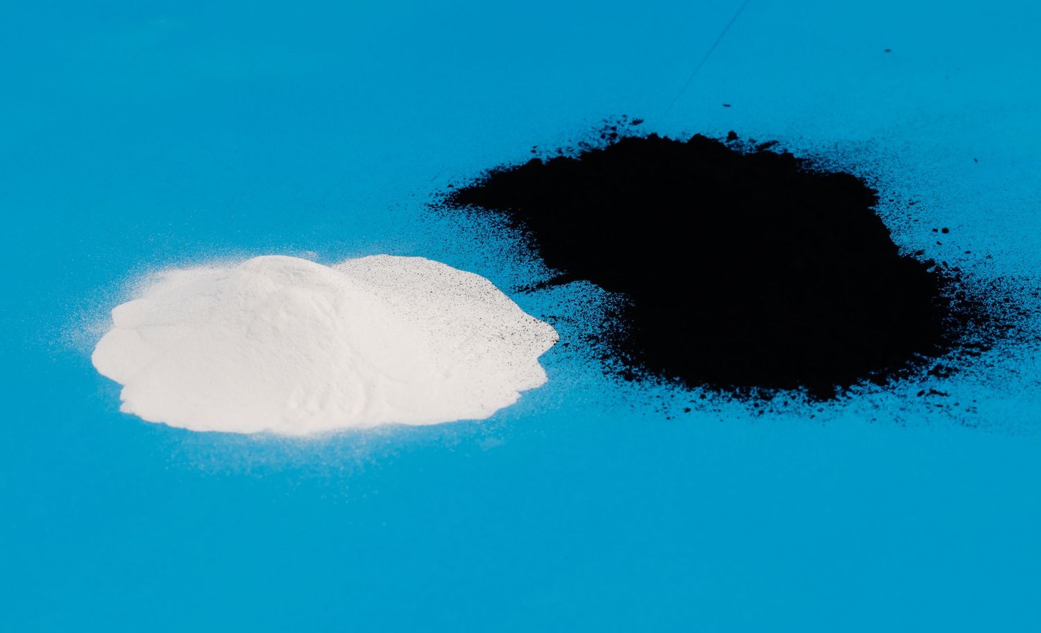 White and black powder samples displayed side by side on a bright blue background for comparison.