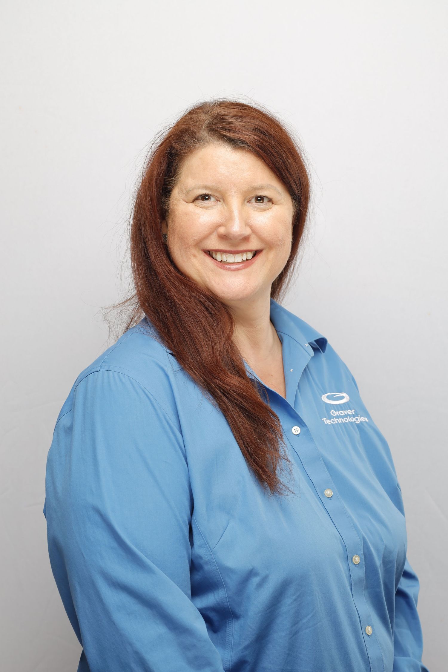 Professional headshot of someone with red hair wearing a light blue company uniform shirt against a gray background.