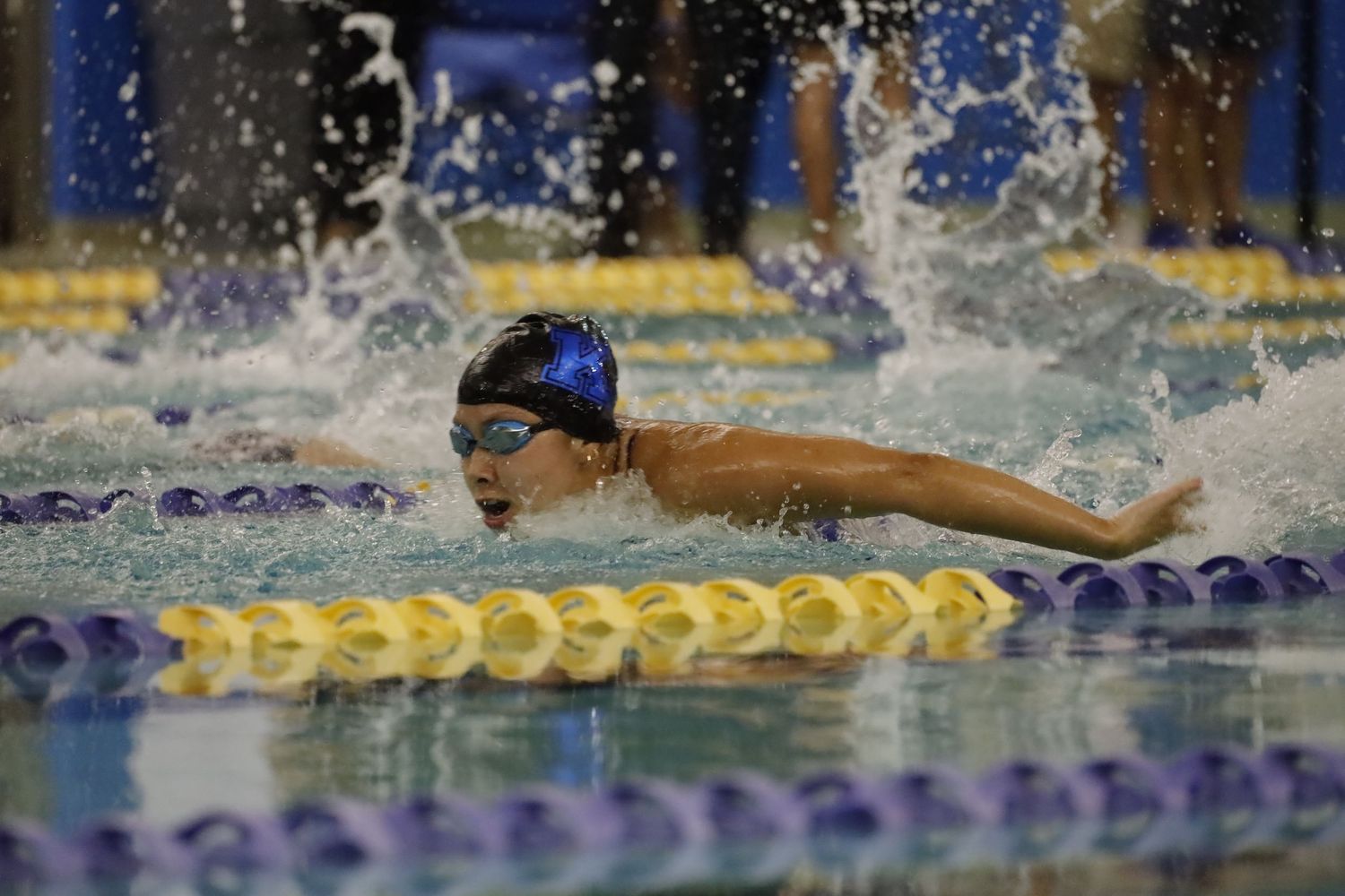 A competitive swimmer performs the butterfly stroke in a pool, creating dramatic water splashes during a race.