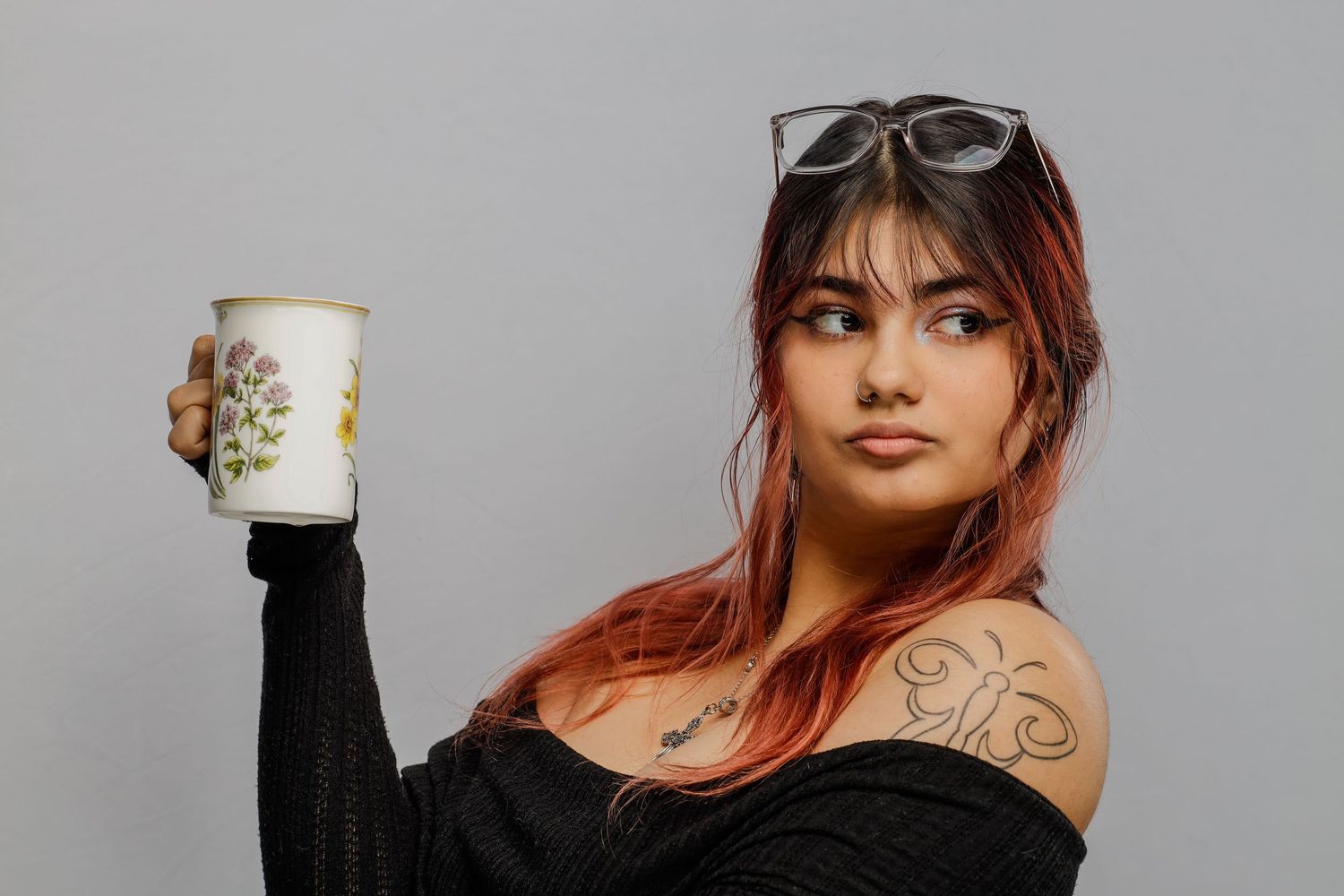 Person with colorful hair holding decorative mug against grey background.