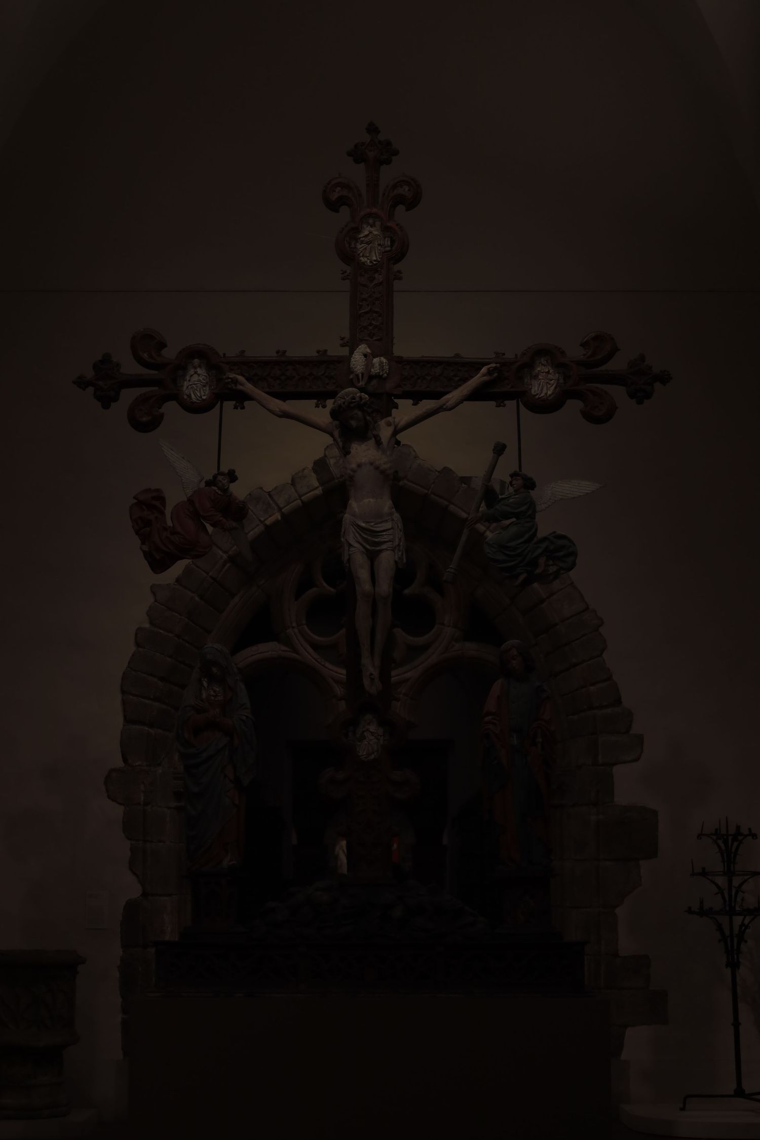 Ornate religious crucifix sculpture silhouetted in dark atmospheric lighting.