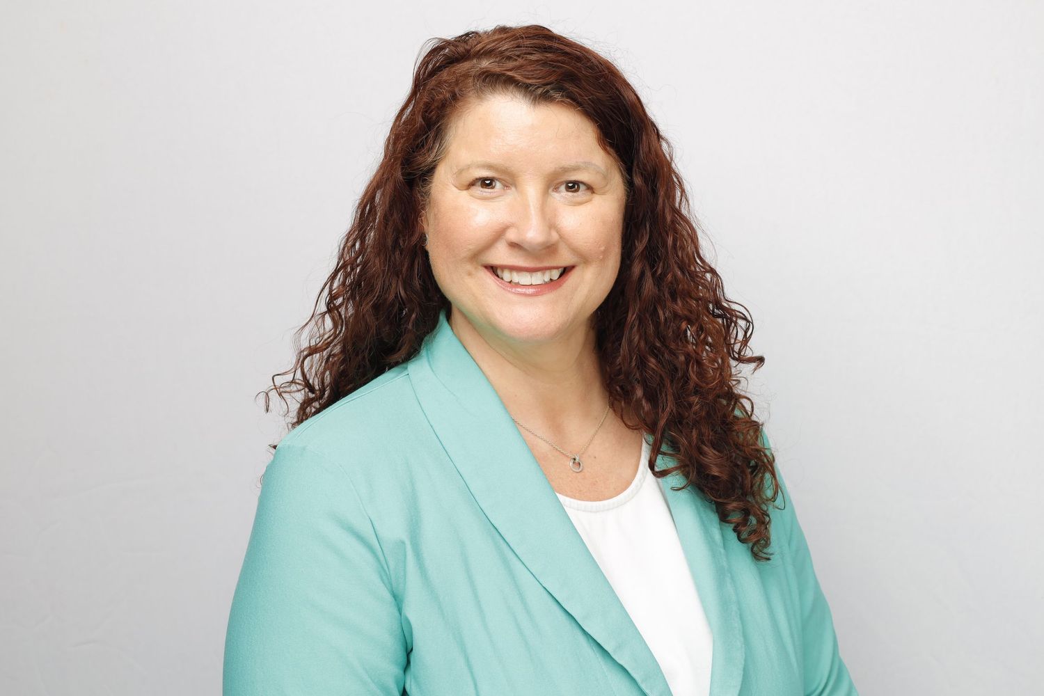 Business portrait of person in turquoise blazer and white shirt smiling warmly with natural curly hair.