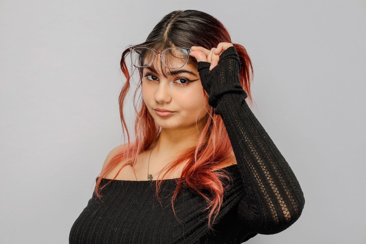 Person wearing a black sweater poses against grey background with vibrant coral-colored hair styled with loose strands.