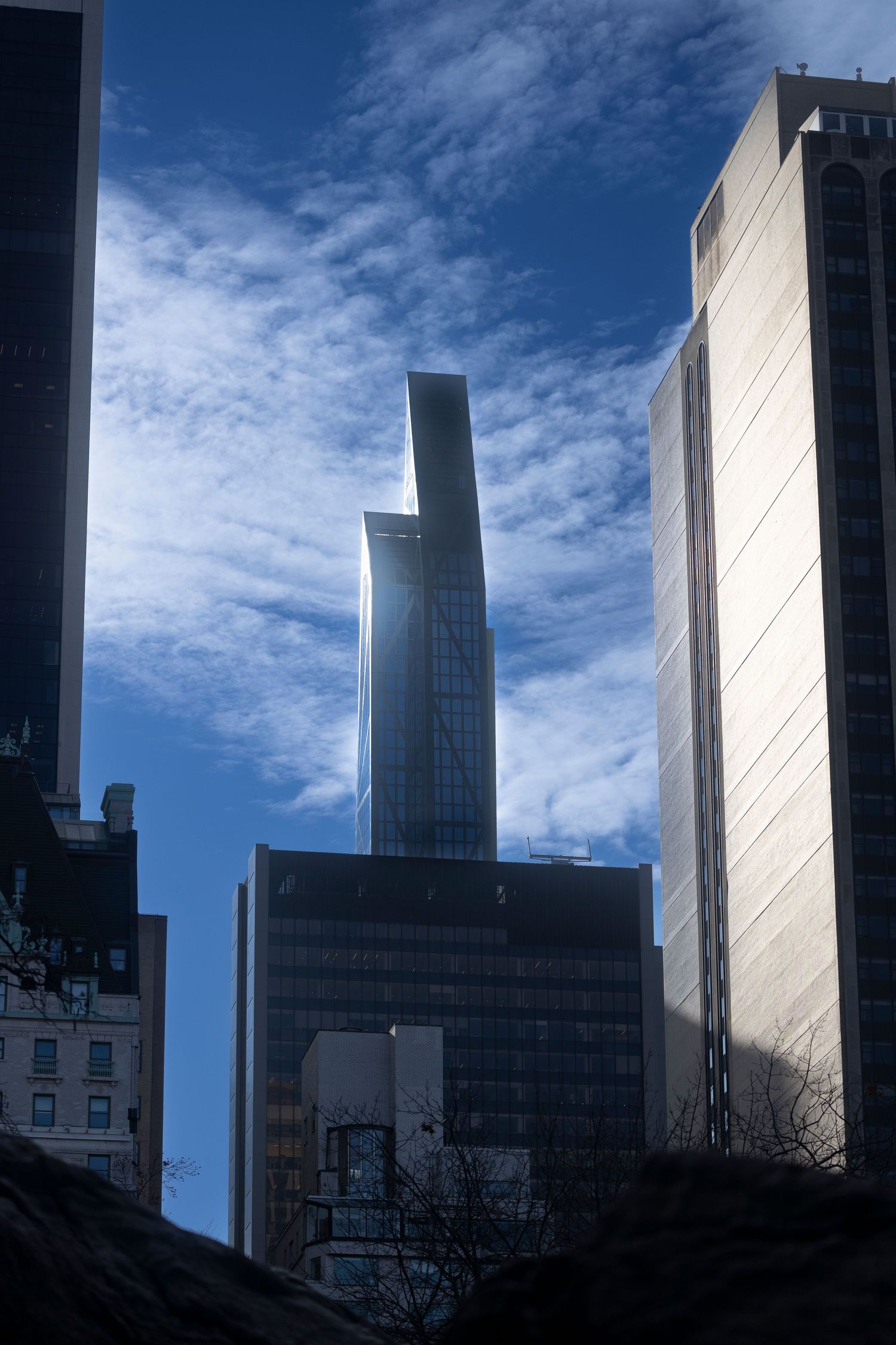 Modern glass skyscraper reaching into blue sky with white clouds between surrounding buildings.