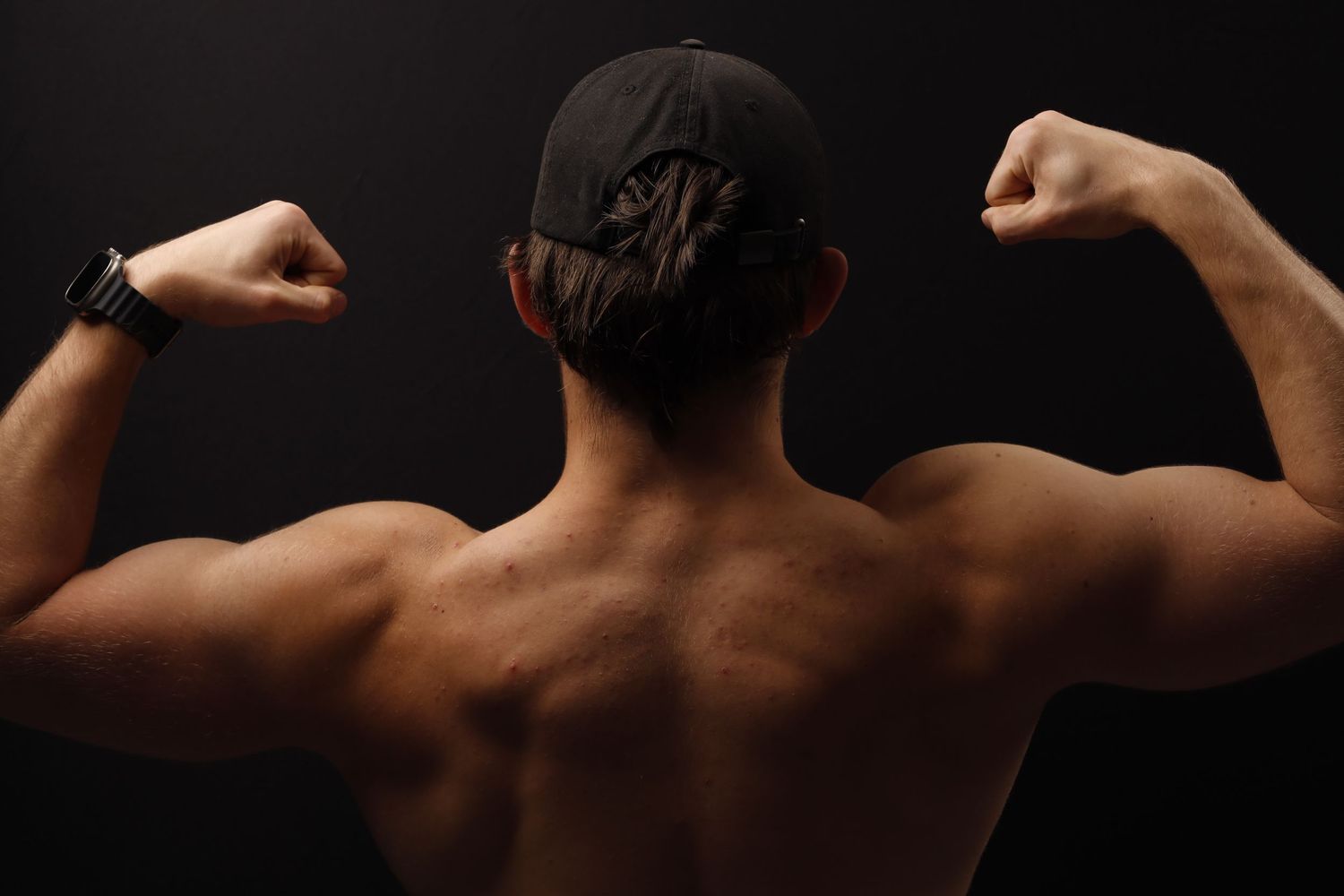 Back view of muscular shoulders and arms flexing against dark background.