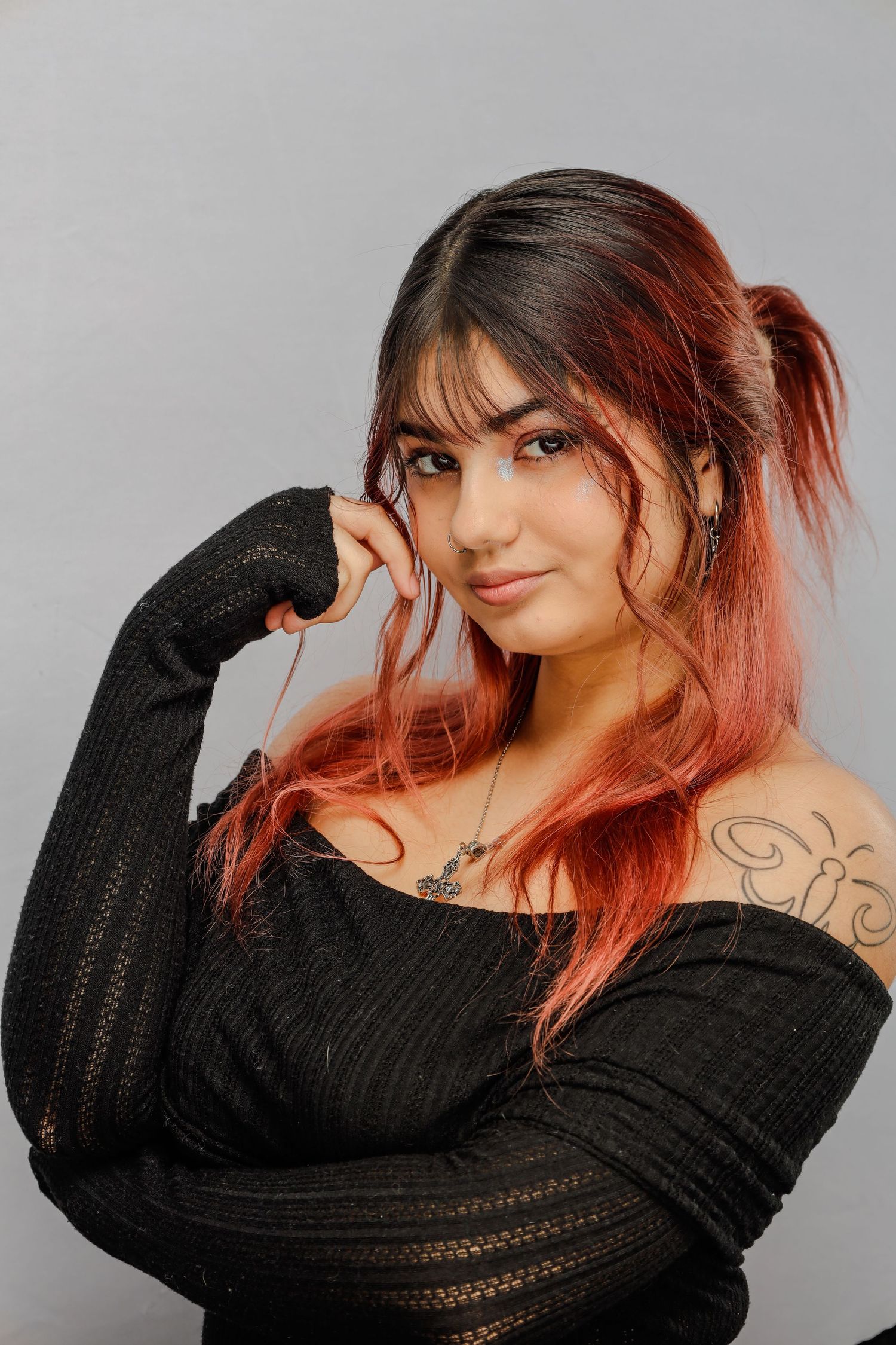 Portrait of someone with pink-tinted hair wearing a black sweater against a gray background.